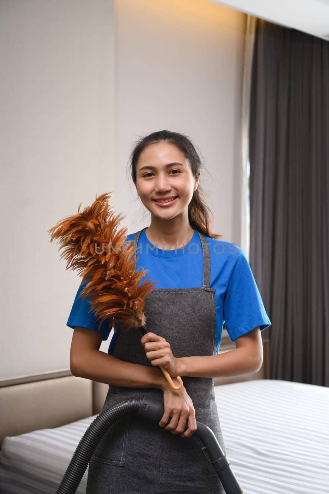 Portrait of female cleaning service worker holding duster and looking at camera.
