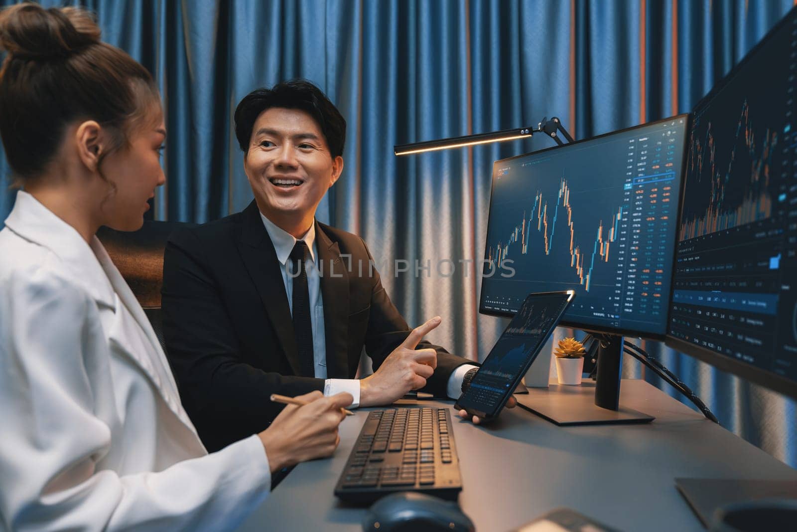 Businessman holding tablet on dynamic stock exchange statistic online showing to partners to share, comparing with high or low point graph on computer screen at night neon modern office. Infobahn.