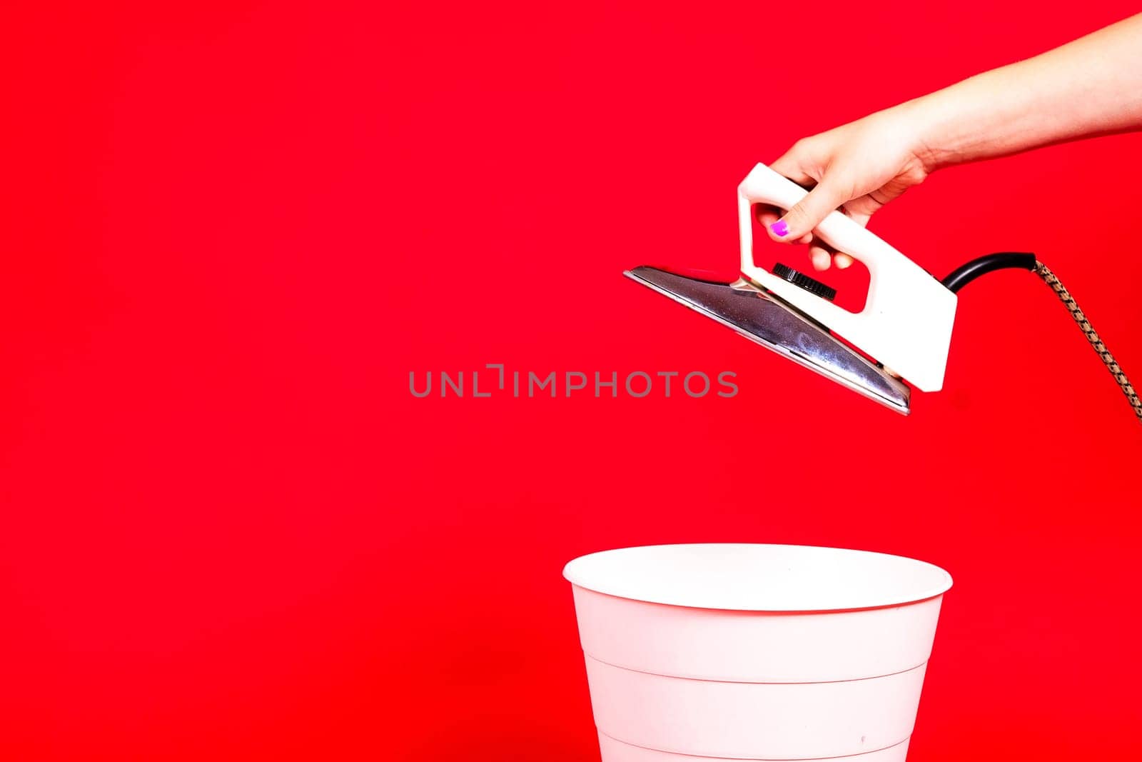 Woman putting iron in a recycle bin on red background