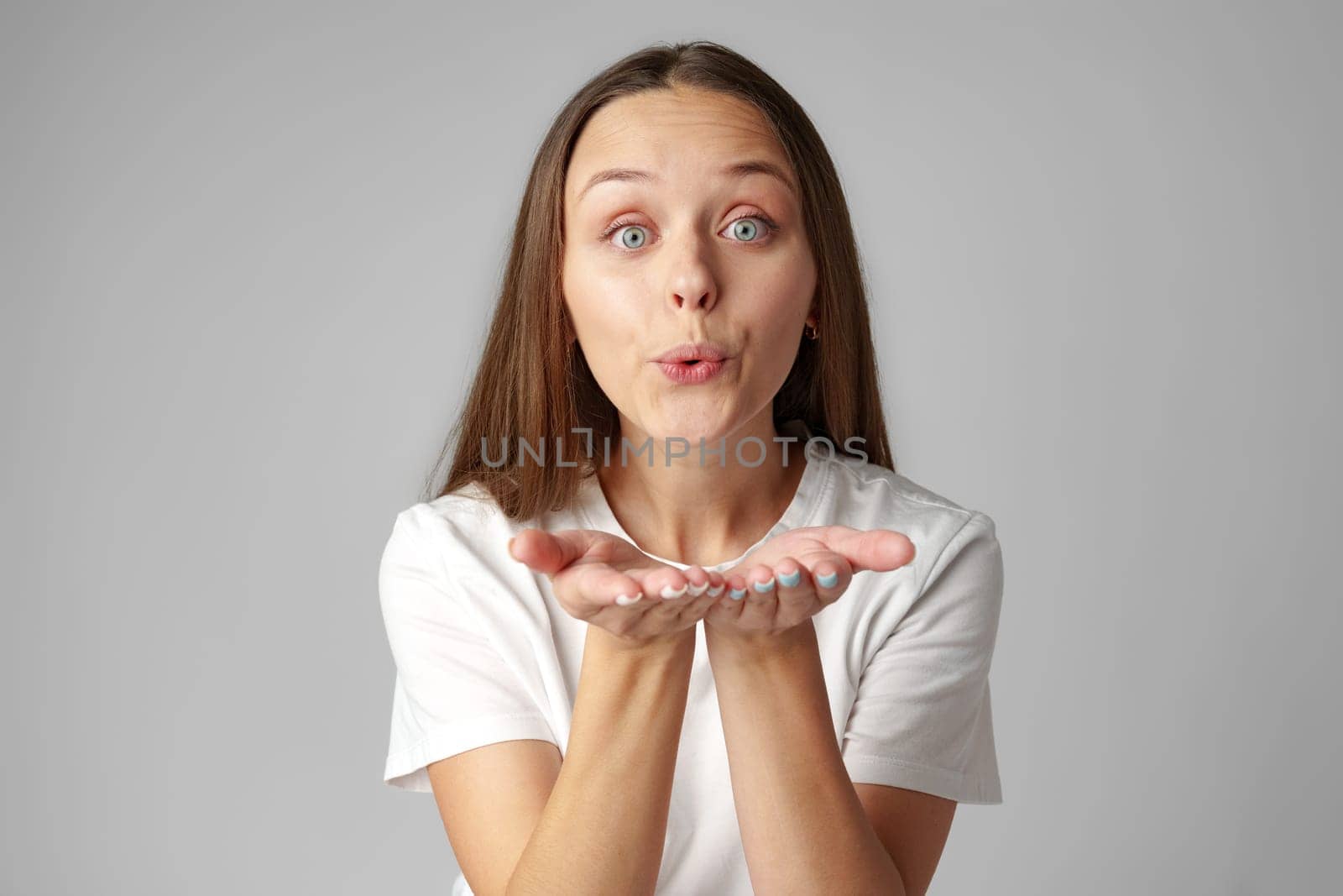 Young woman blowing a kiss to camera on gray background studio shot