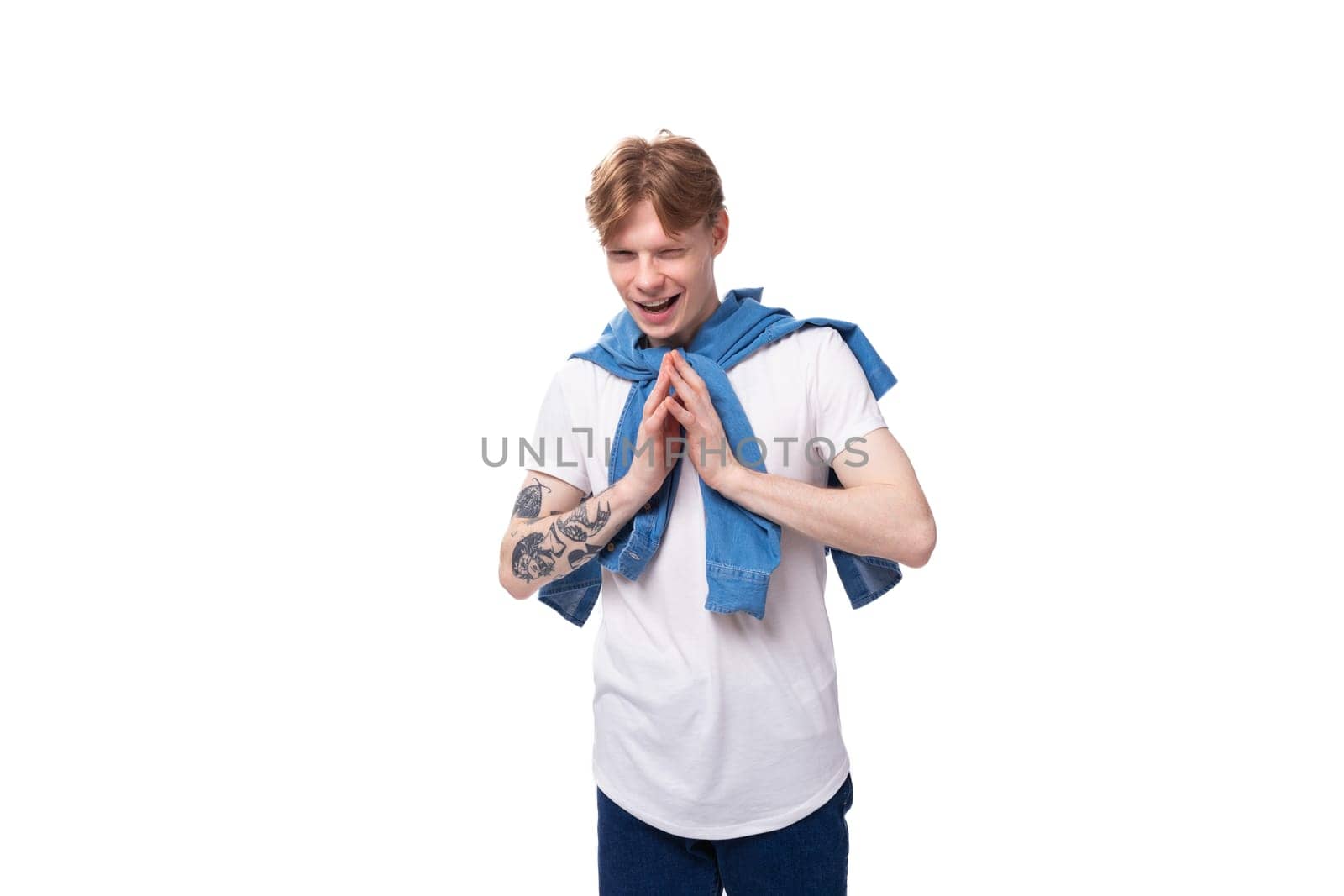 young emotional handsome slender red-haired man with a tattoo on his arms is dressed in a stylish blue shirt.