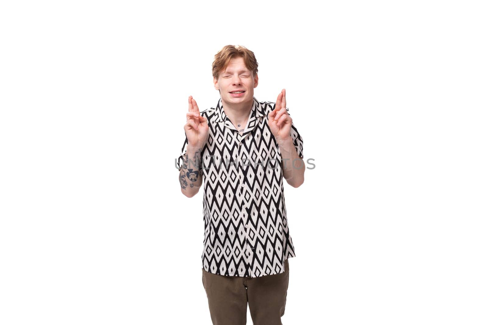 a young caucasian man with red hair with a tattoo dressed in a summer black and white shirt is waiting and thinking against the background with copy space.