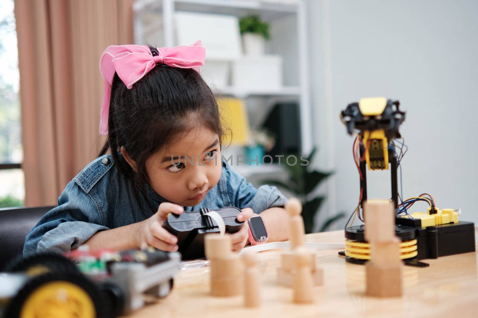 A primary school girl focuses on operating a robotic arm with a remote control, demonstrating STEM education in action.