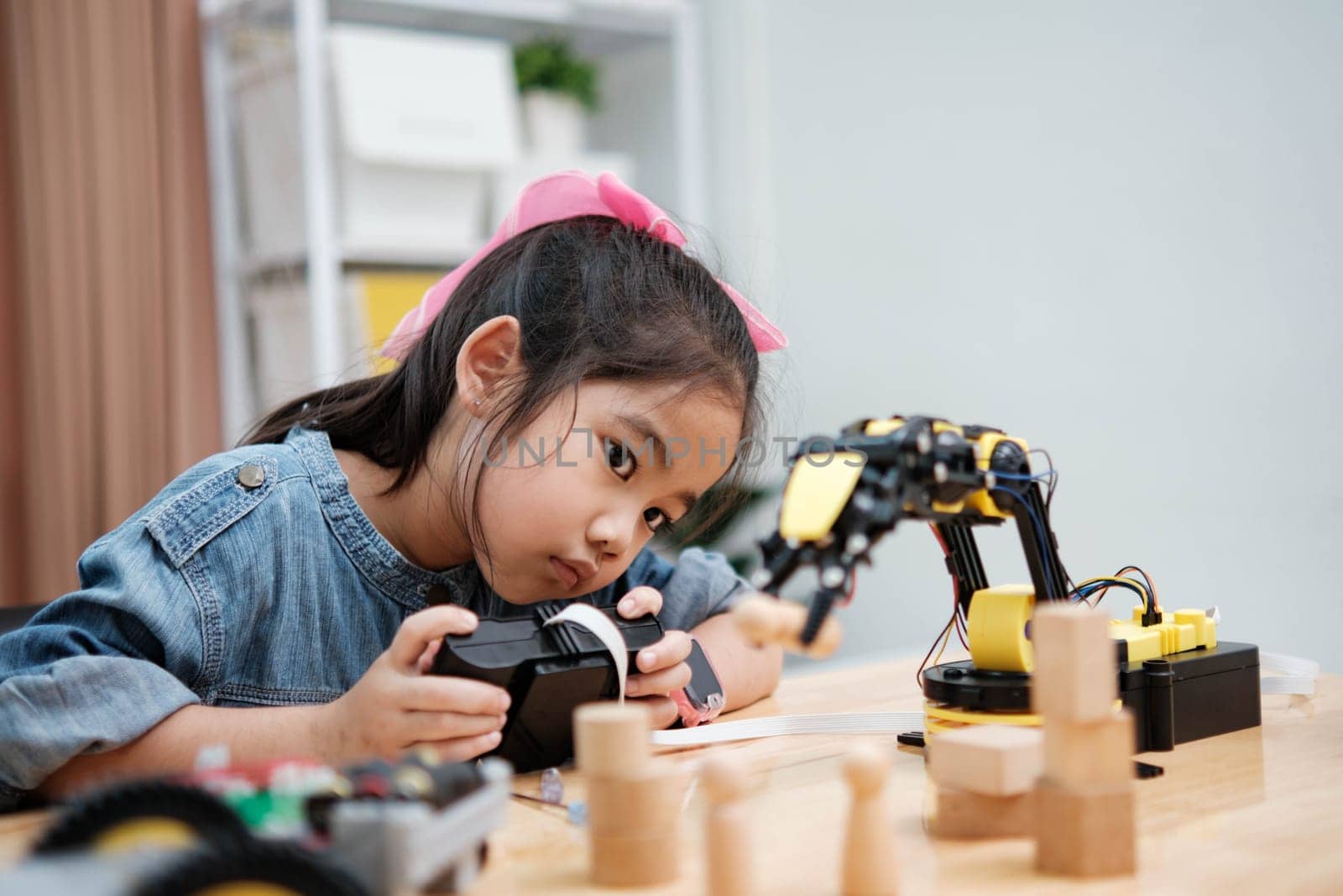 A primary school girl focuses on operating a robotic arm with a remote control, demonstrating STEM education in action.