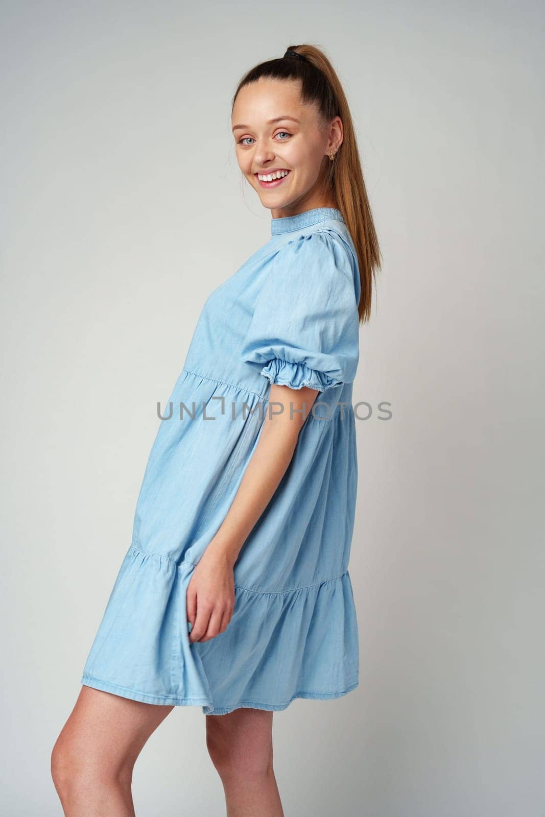 Young happy smiling woman in a light blue dress on a gray background close up