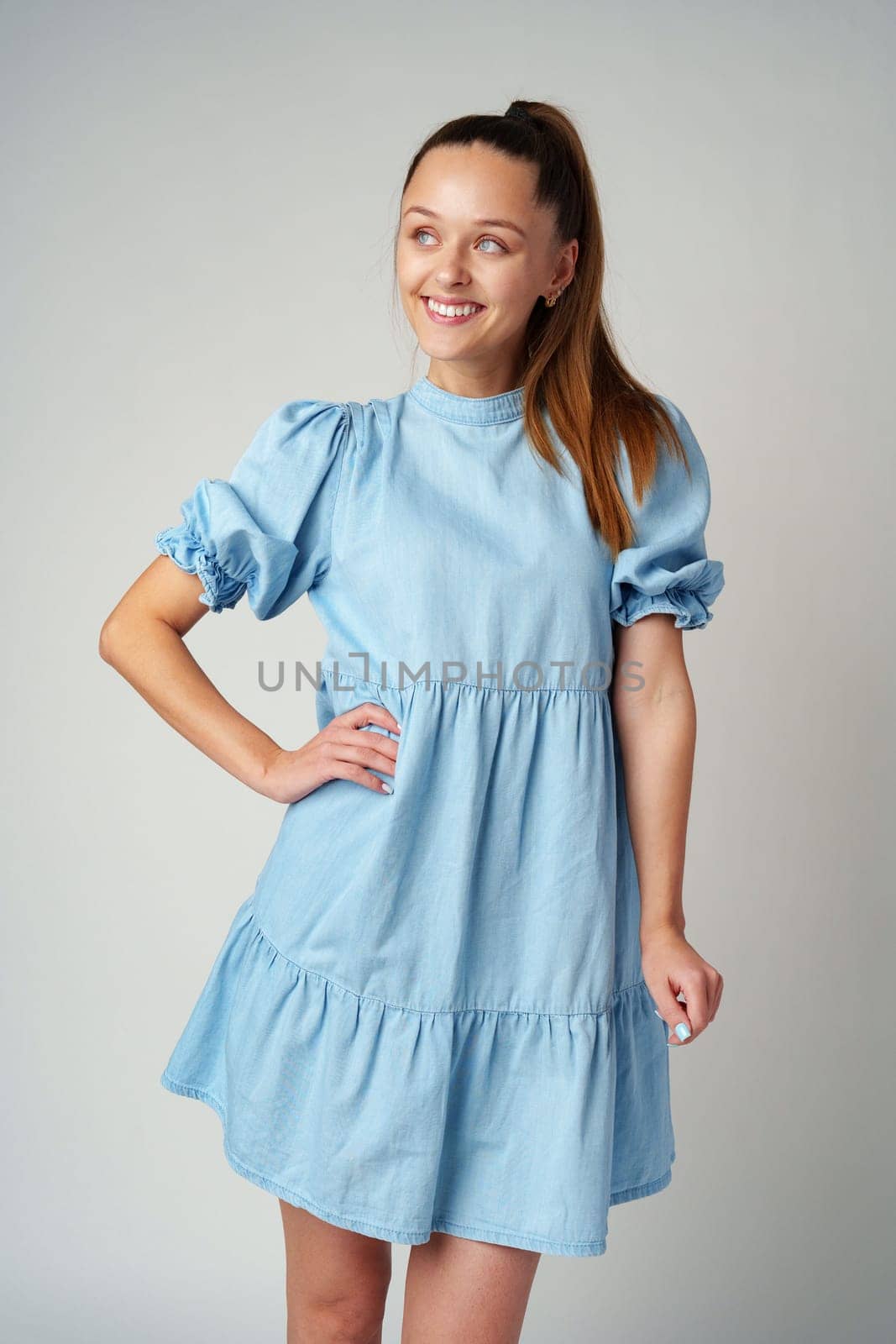 Young happy smiling woman in a light blue dress on a gray background close up