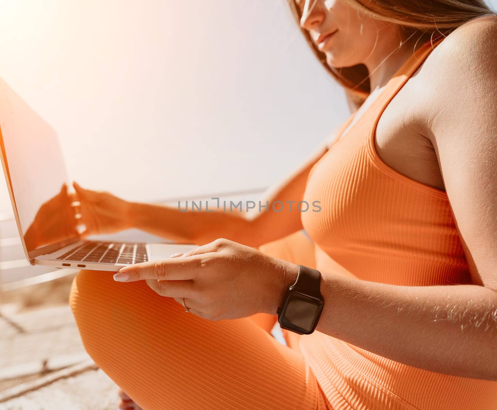 Digital nomad, Business woman working on laptop by the sea. Pretty lady typing on computer by the sea at sunset, makes a business transaction online from a distance. Freelance, remote work on vacation