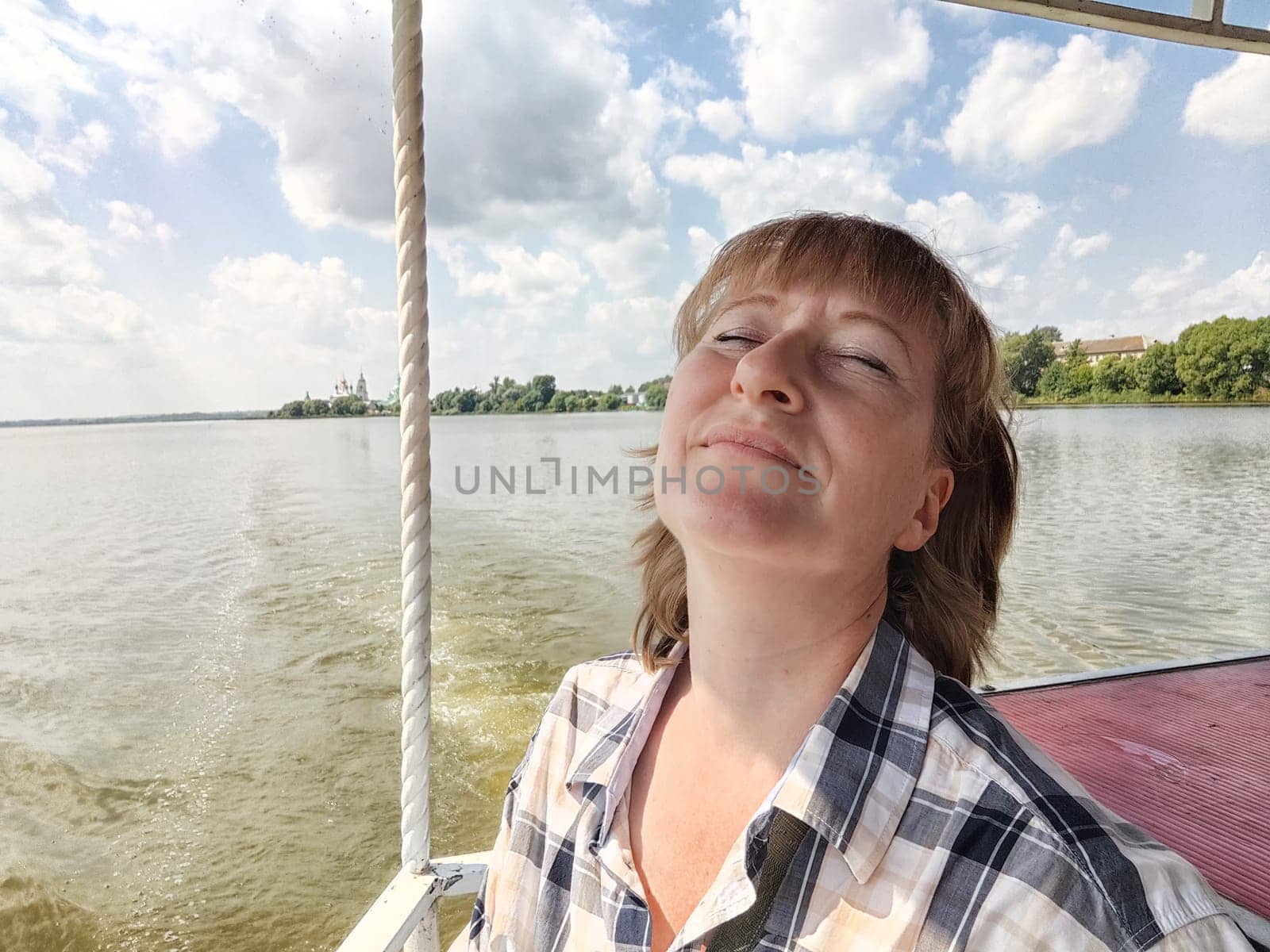 Happy cheerful middle aged woman taking selfie on nature outdoors and sun with water of lake or river on the background in summer day