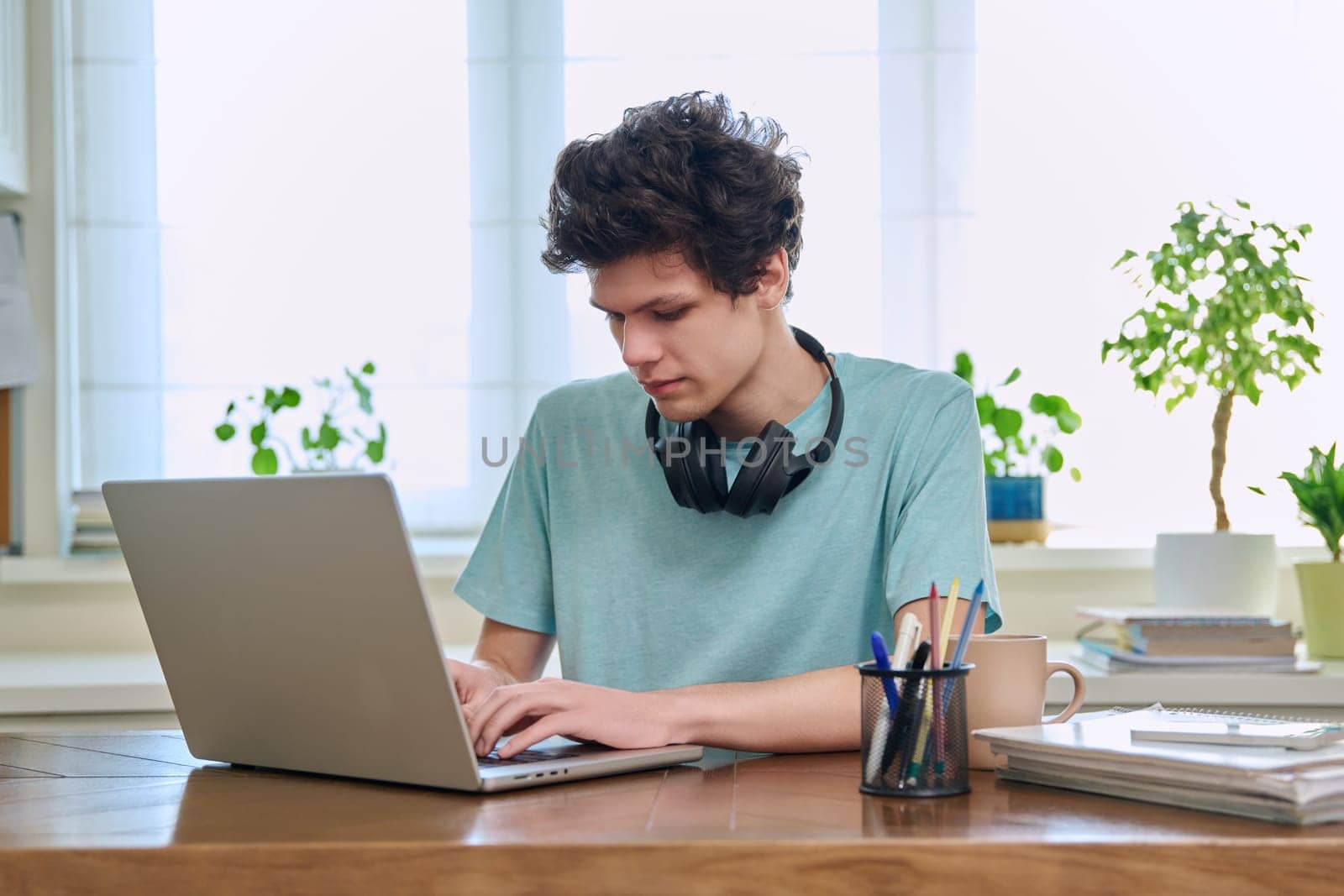 Young male college student sitting at desk at home using laptop by VH-studio