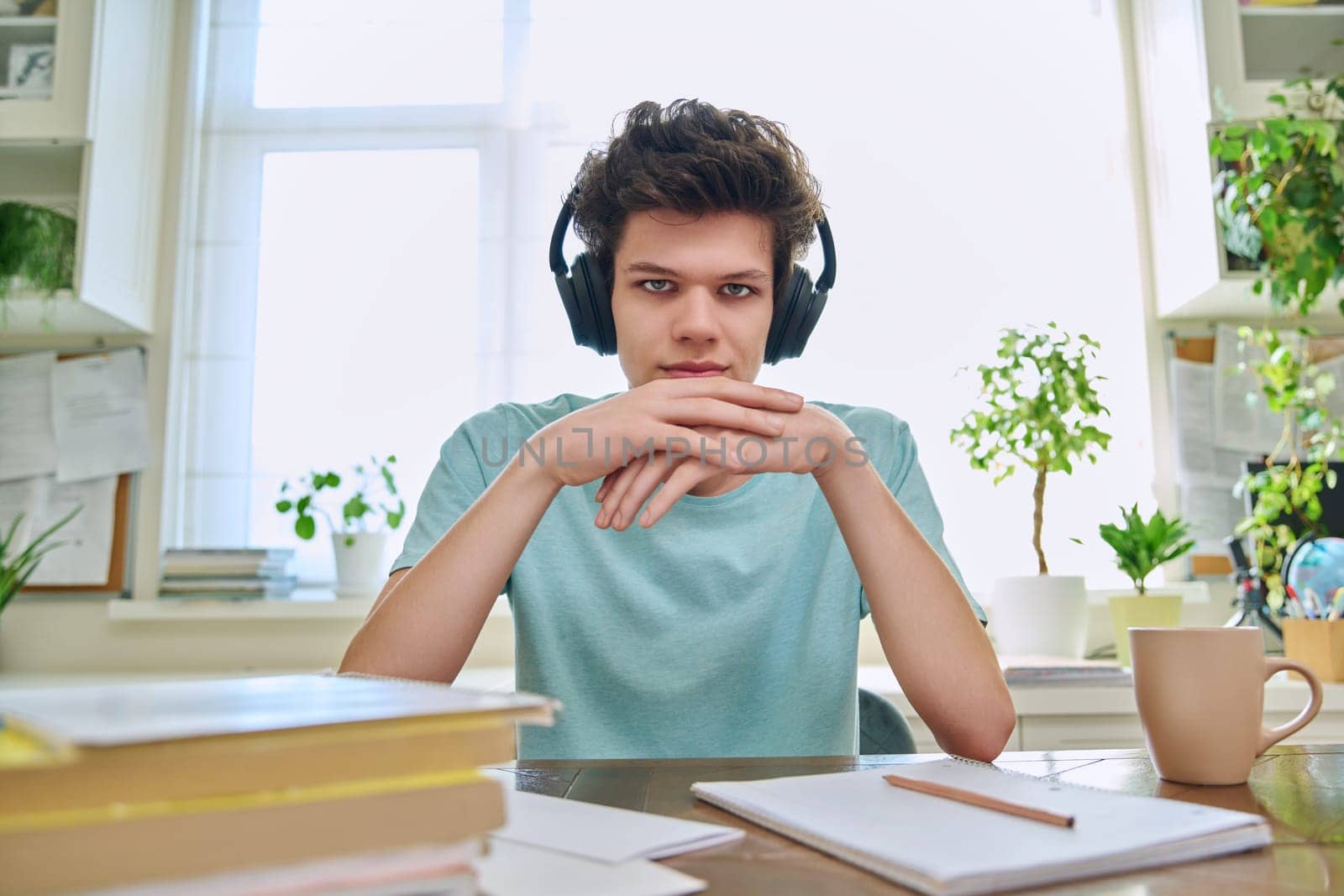 Webcam view of college student guy wearing headphones, talking looking at camera, sitting at desk in home. Young male studying online, video chat call conference, e-learning technology education