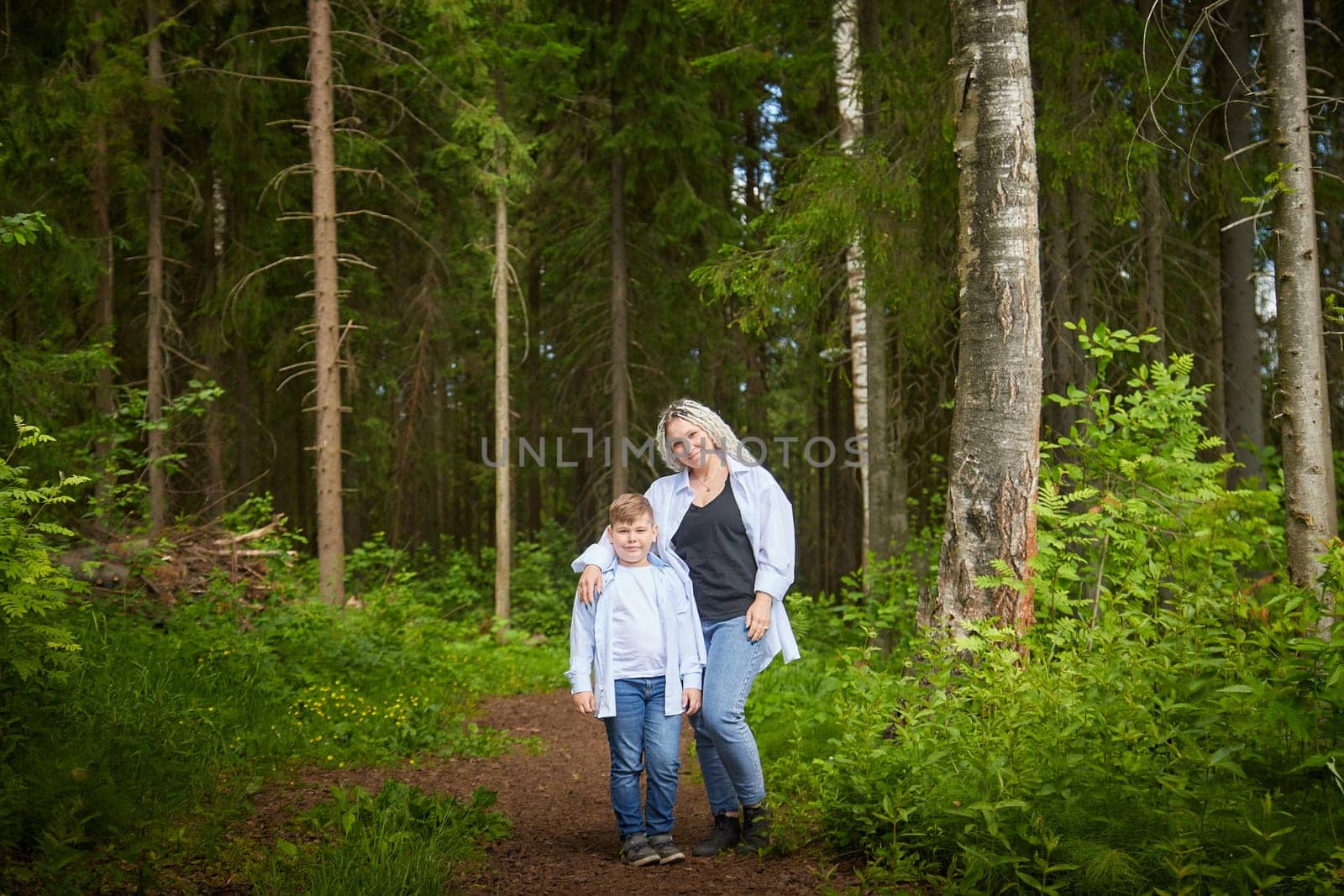 Funny mother with dreadlocks and fat boy happy walking in the forest on a sunny summer day