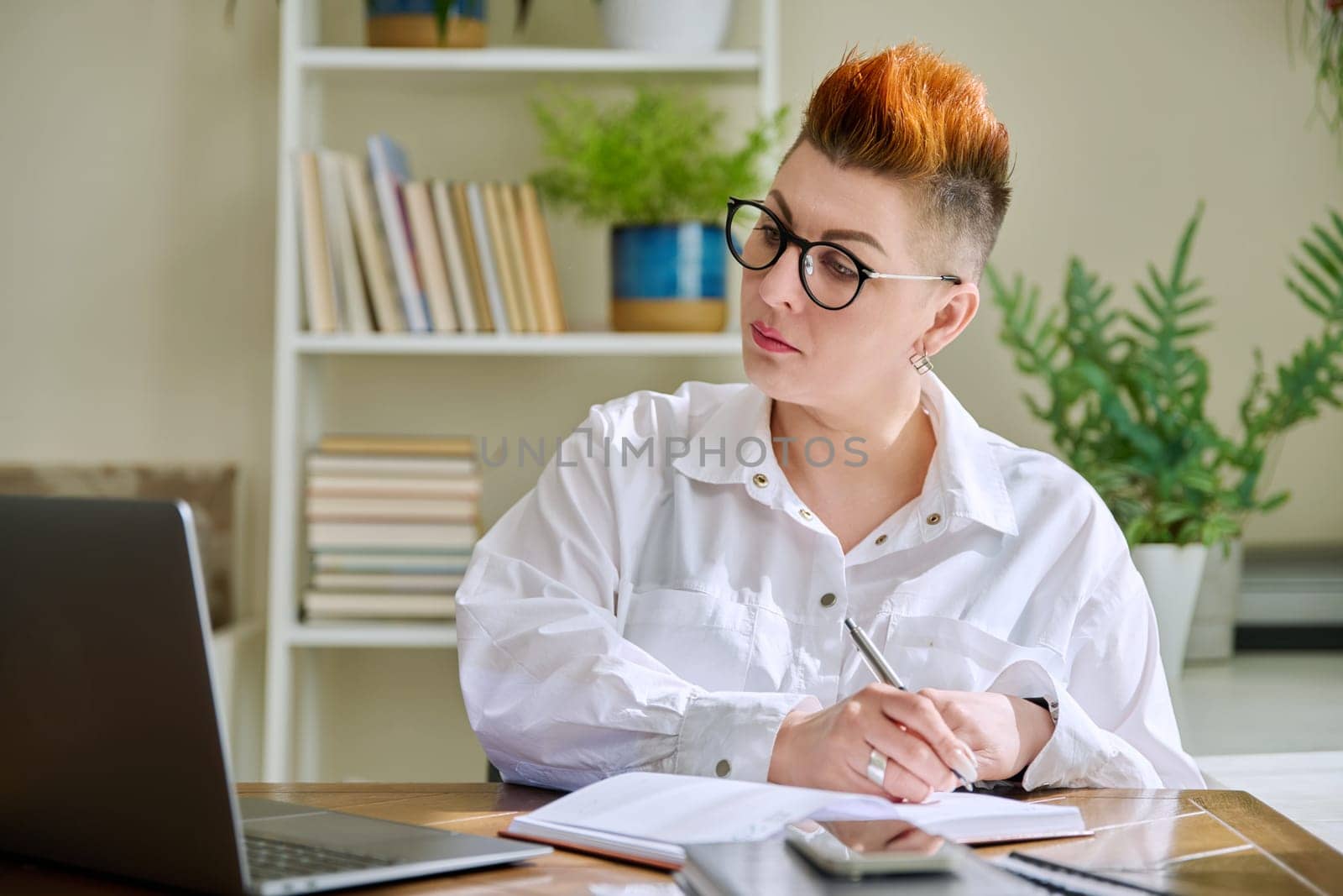 Middle aged woman working with computer papers, remote workplace in home office by VH-studio