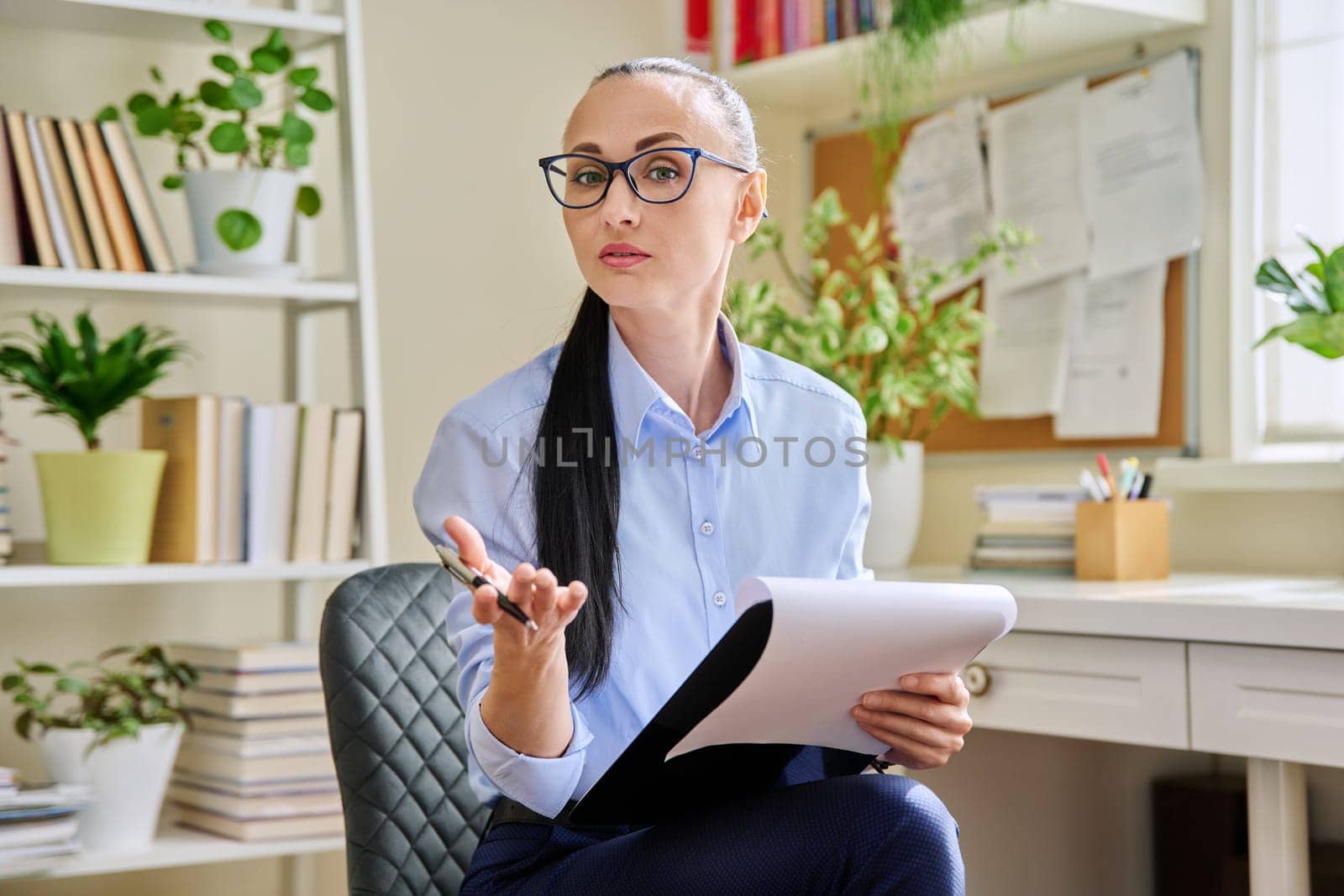 Portrait of female psychologist with clipboard at workplace in office by VH-studio