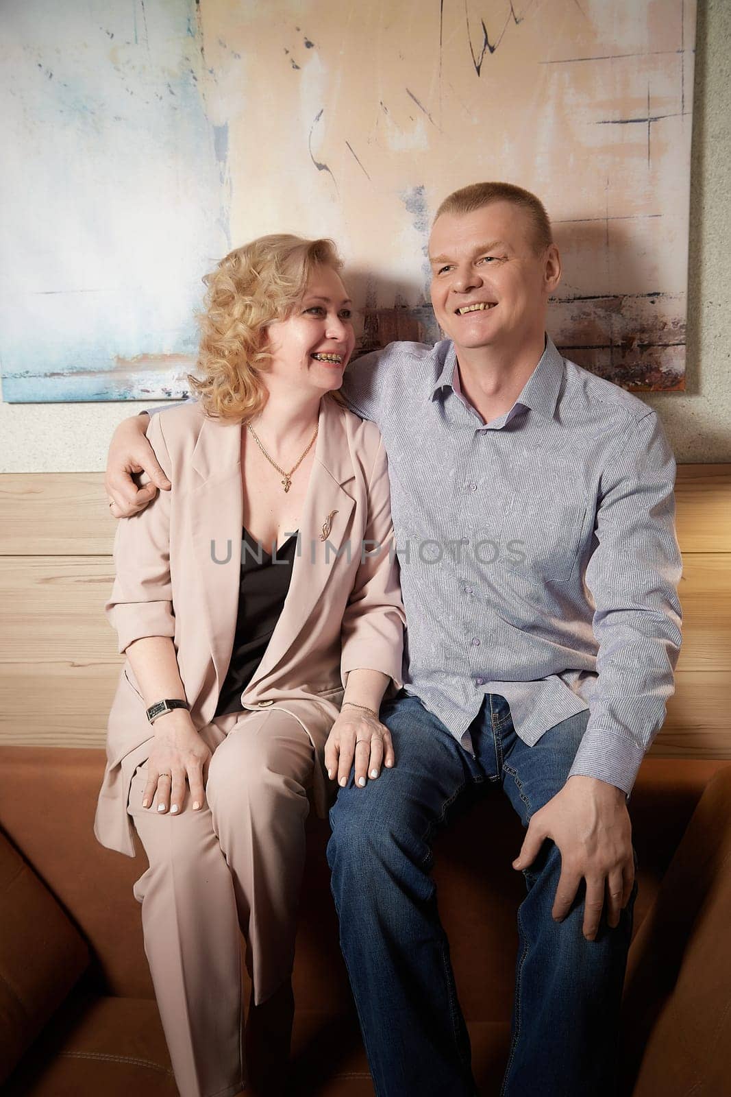 Loving adult couple communicates and embraces privately in the living room or in hotel. The woman is wearing business formal suit and man is wearing jeans and a shirt, indicating a close relationship by keleny