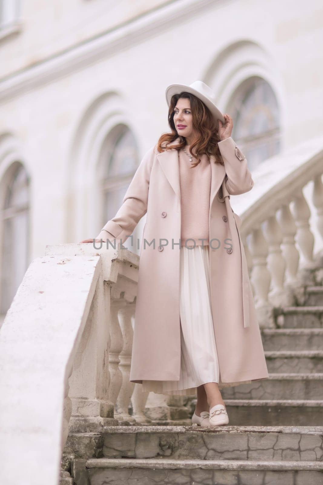 woman in elegant coat and hat against an intricate architectural backdrop, harmoniously blending modern fashion with historical allure. The soft daylight adds to its timeless appeal