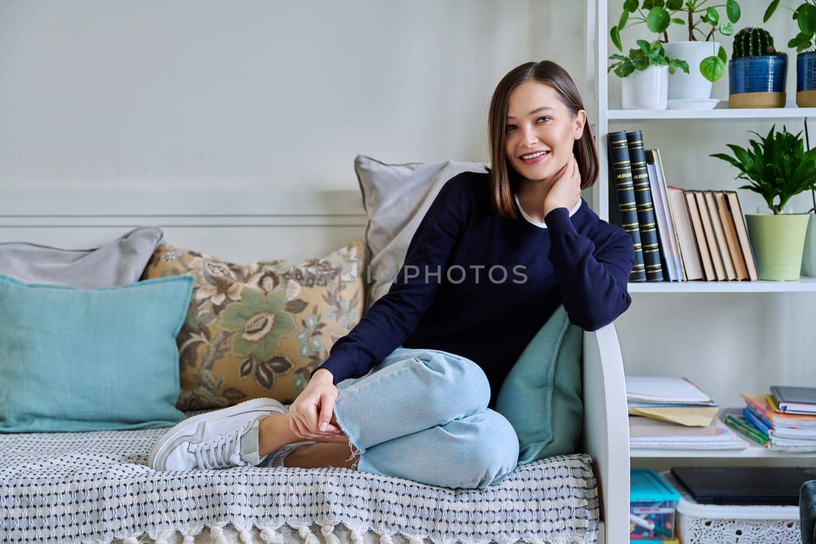 Portrait of young attractive smiling woman in home interior. Happy cheerful relaxed 20s female looking at camera, sitting on couch. Beauty, youth, happiness, health, lifestyle concept