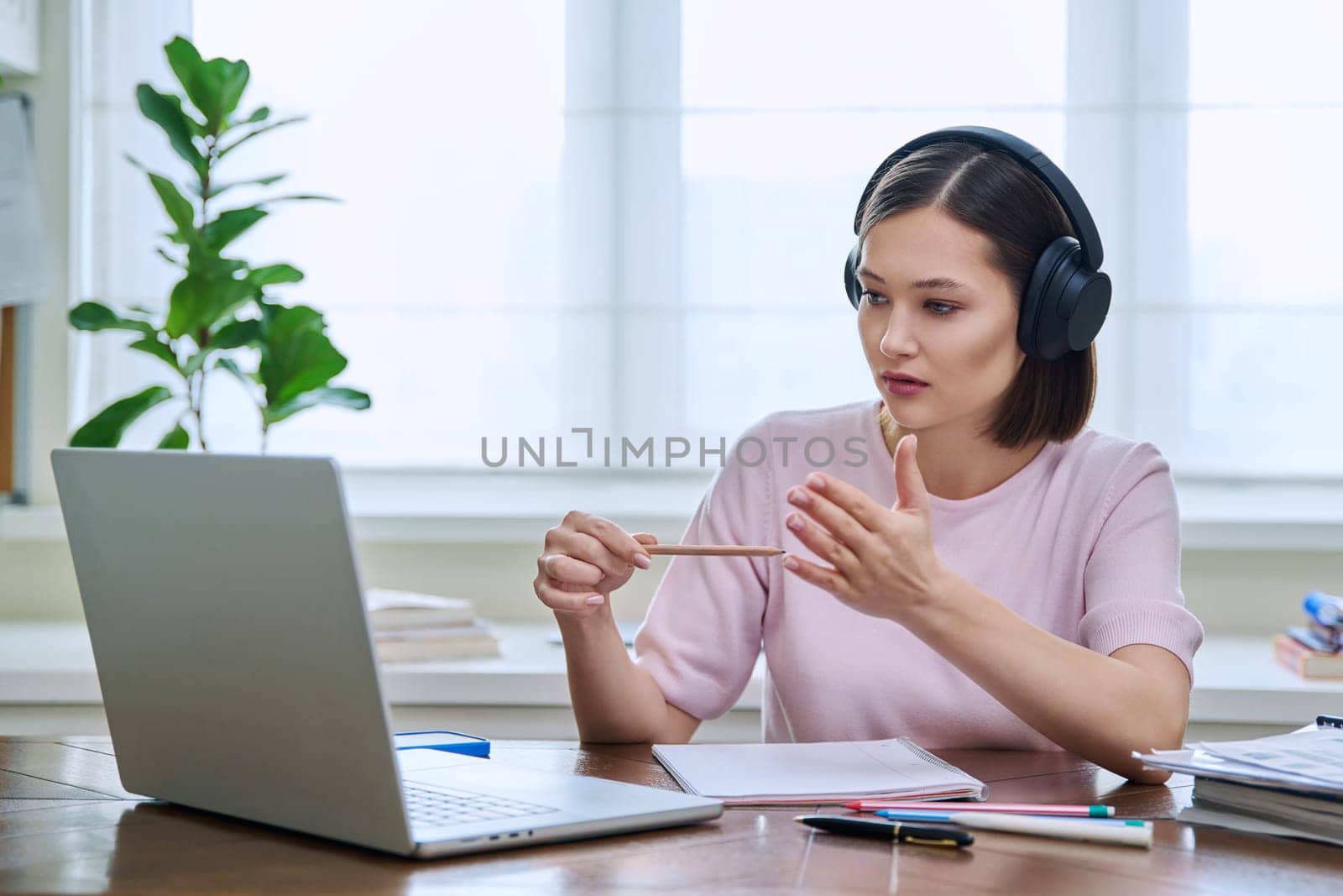 Young female college university student in headphones talking studying using laptop computer for video chat conference call sitting at home. Internet online remote lessons webinars education training