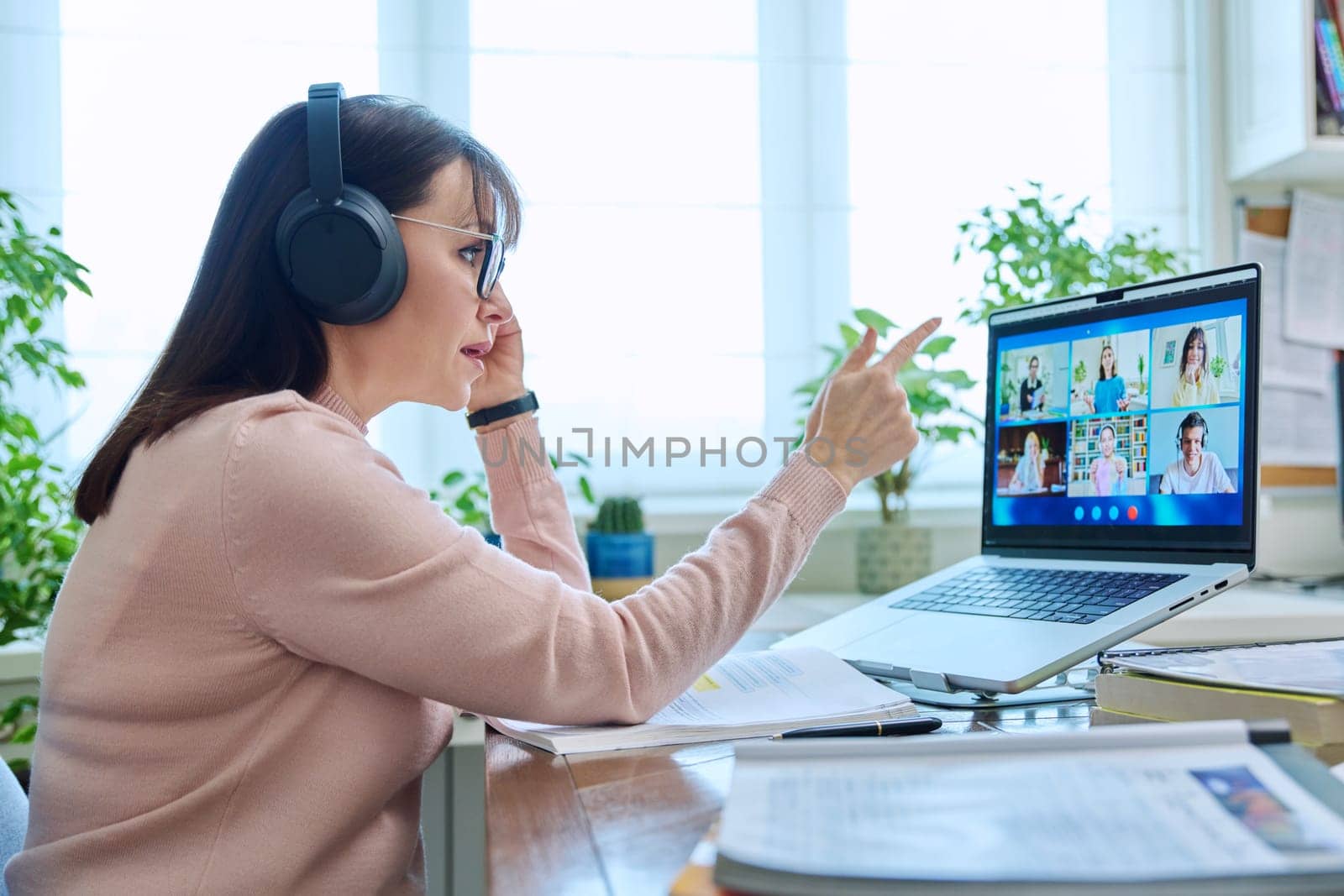 Woman teacher in headphones teaching online, high school students on computer screen by VH-studio