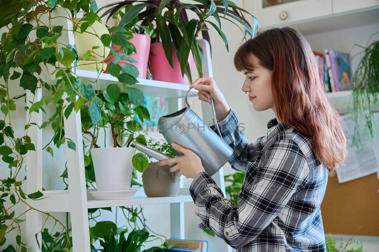 Young woman watering pots with plants from watering can, home interior. Home landscaping, eco green trends, lifestyle concept