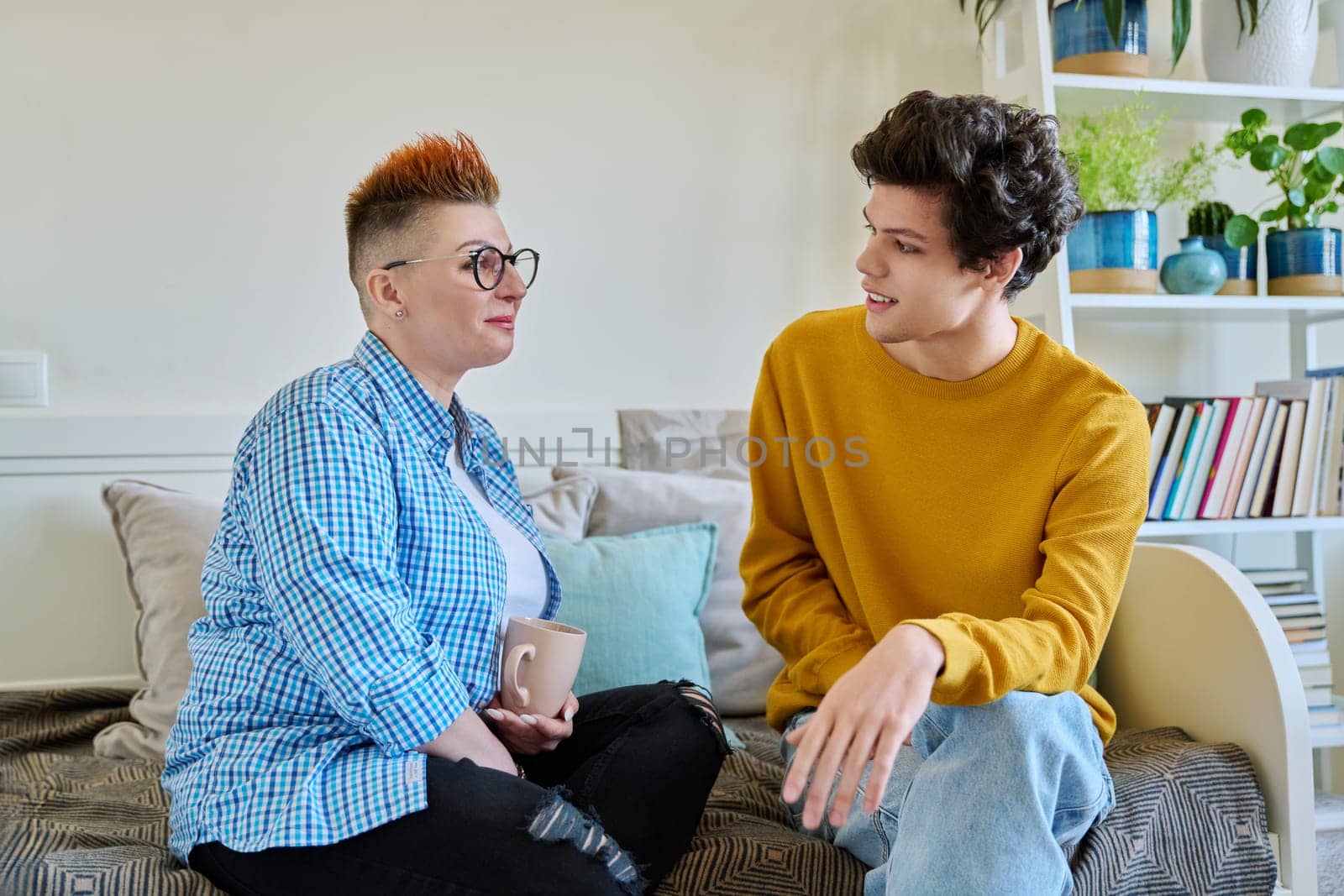Happy middle-aged mother and son 19-20 years old, talking sitting together at home by VH-studio