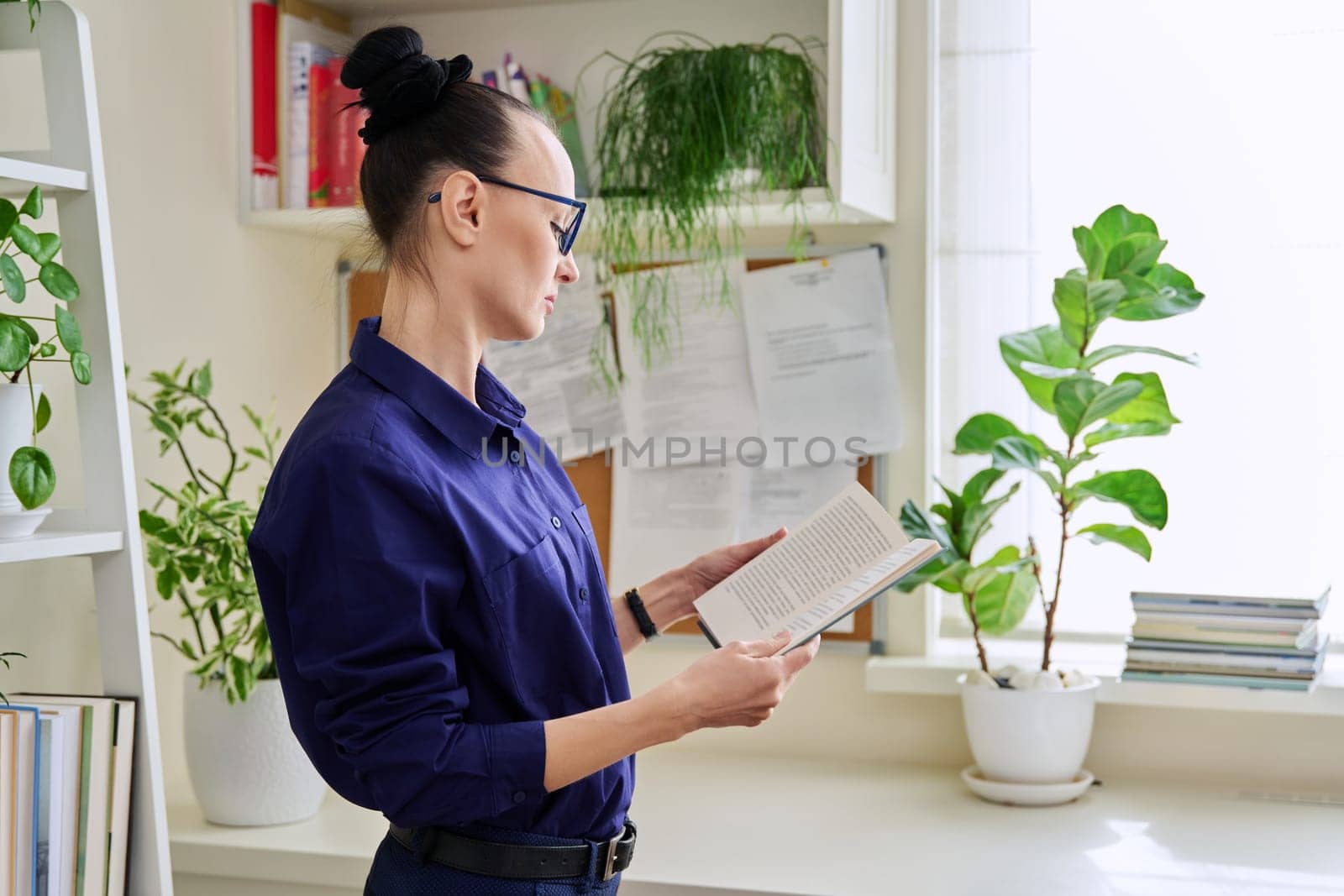 Middle-aged woman reading fiction book at home, at home near window by VH-studio