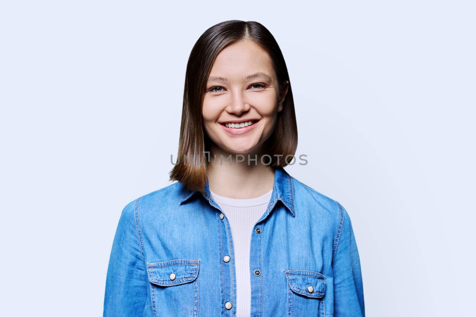 Young beautiful cheerful woman on white studio background. Smiling attractive 20s female in denim looking at camera. Lifestyle, fashion beauty style, youth business work services, education, healthcare