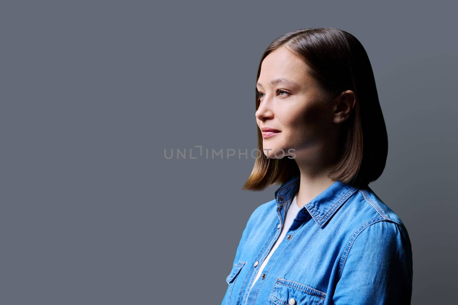 Profile portrait of young smiling woman on grey background by VH-studio