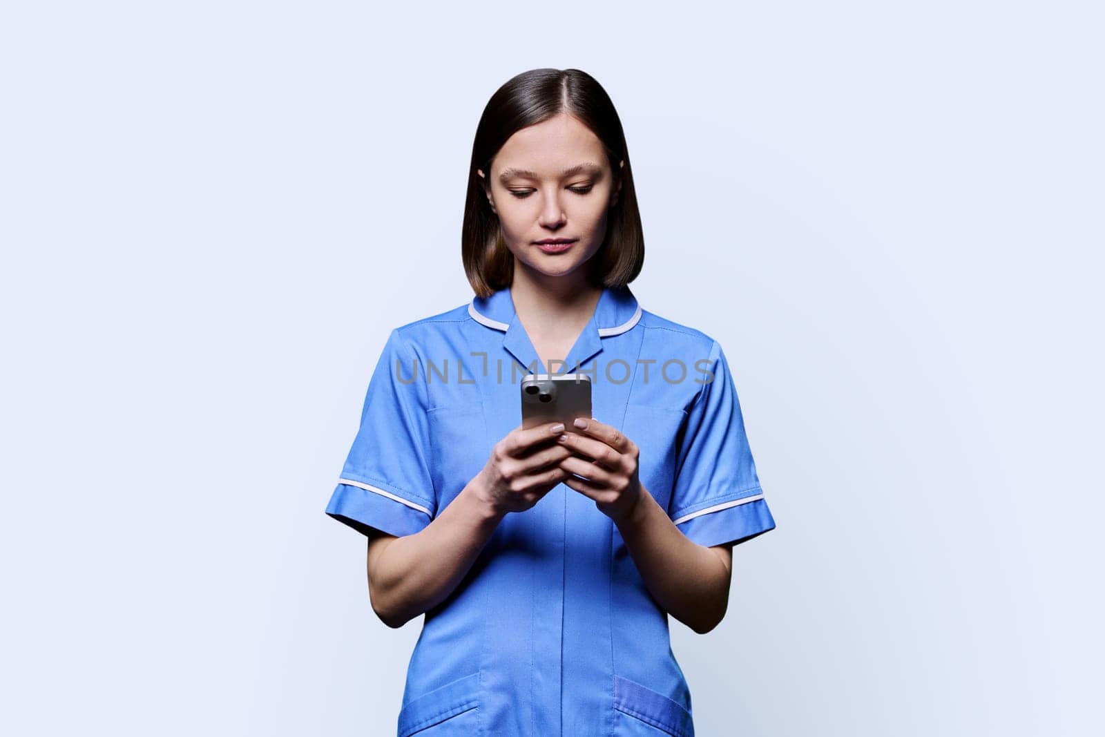 Serious young female nurse using smartphone, on white studio background. Mobile apps applications, technologies in medical services, health, professional assistance, medical care concept