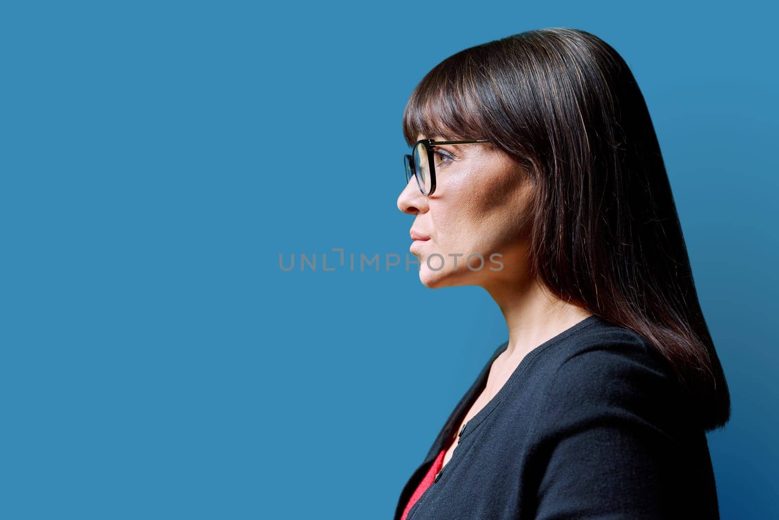 Profile view of middle aged serious woman looking forward, blue studio background, copy space for advertising image text. Mature business confident successful female. Marketing sales services, people