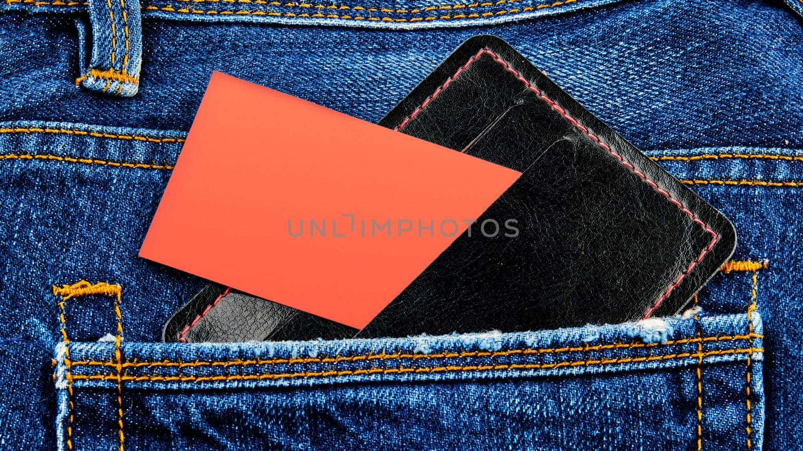 A close-up business card on the front pocket. An empty orange card with a copy space in the pocket of your jeans.