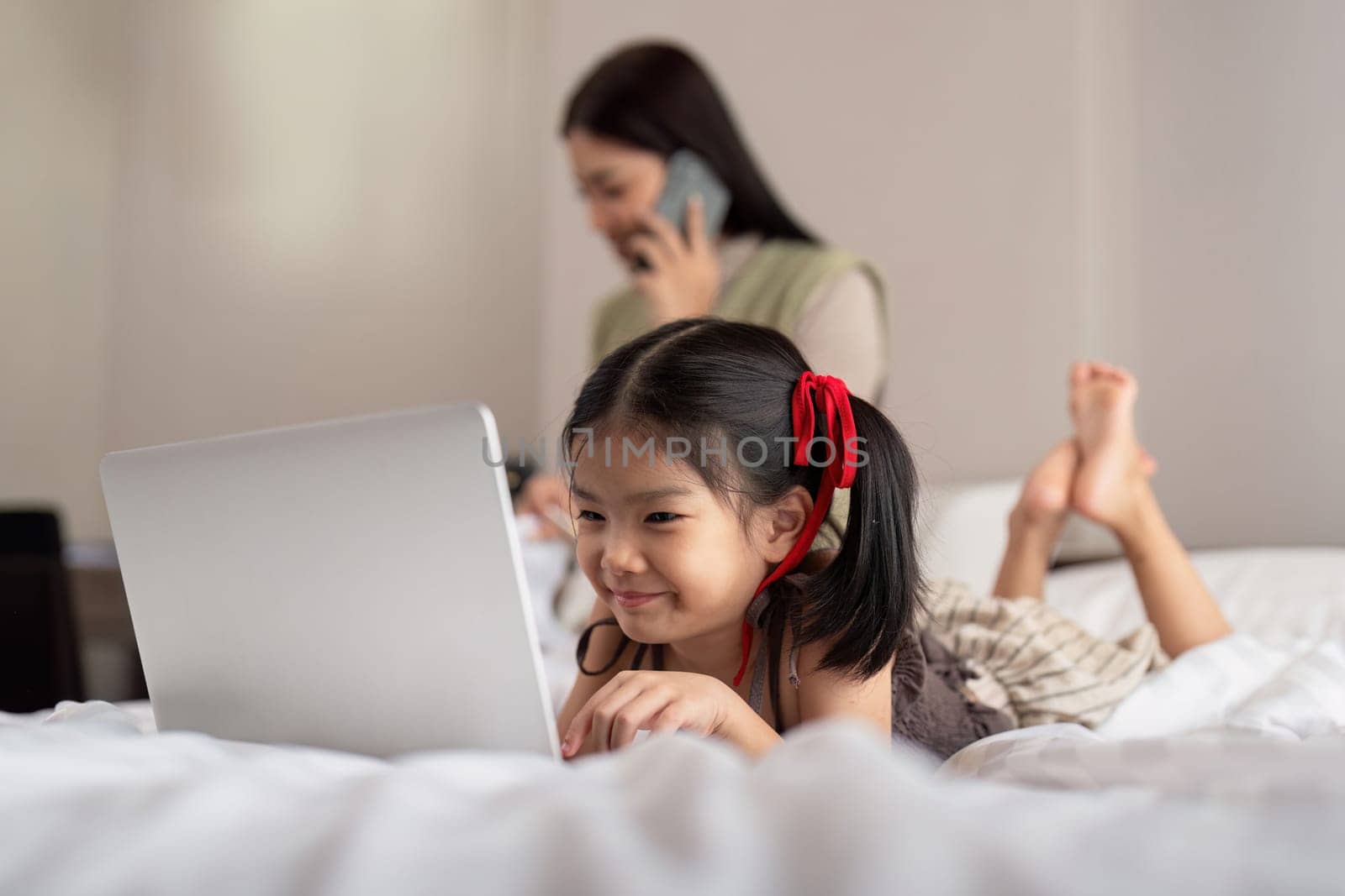 Asian happy young mother and baby lifestyle working on laptop, Mother working on bed with daughter learning technology on laptop computer on bedroom bed.