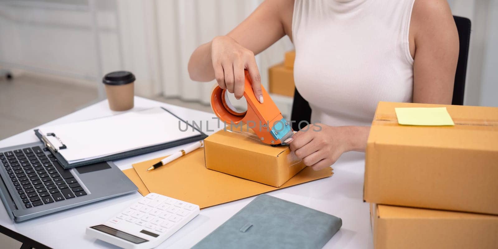 Woman asian use scotch tape to attach parcel boxes to prepare goods for the process of packaging, shipping, online sale internet marketing ecommerce concept startup business idea by nateemee