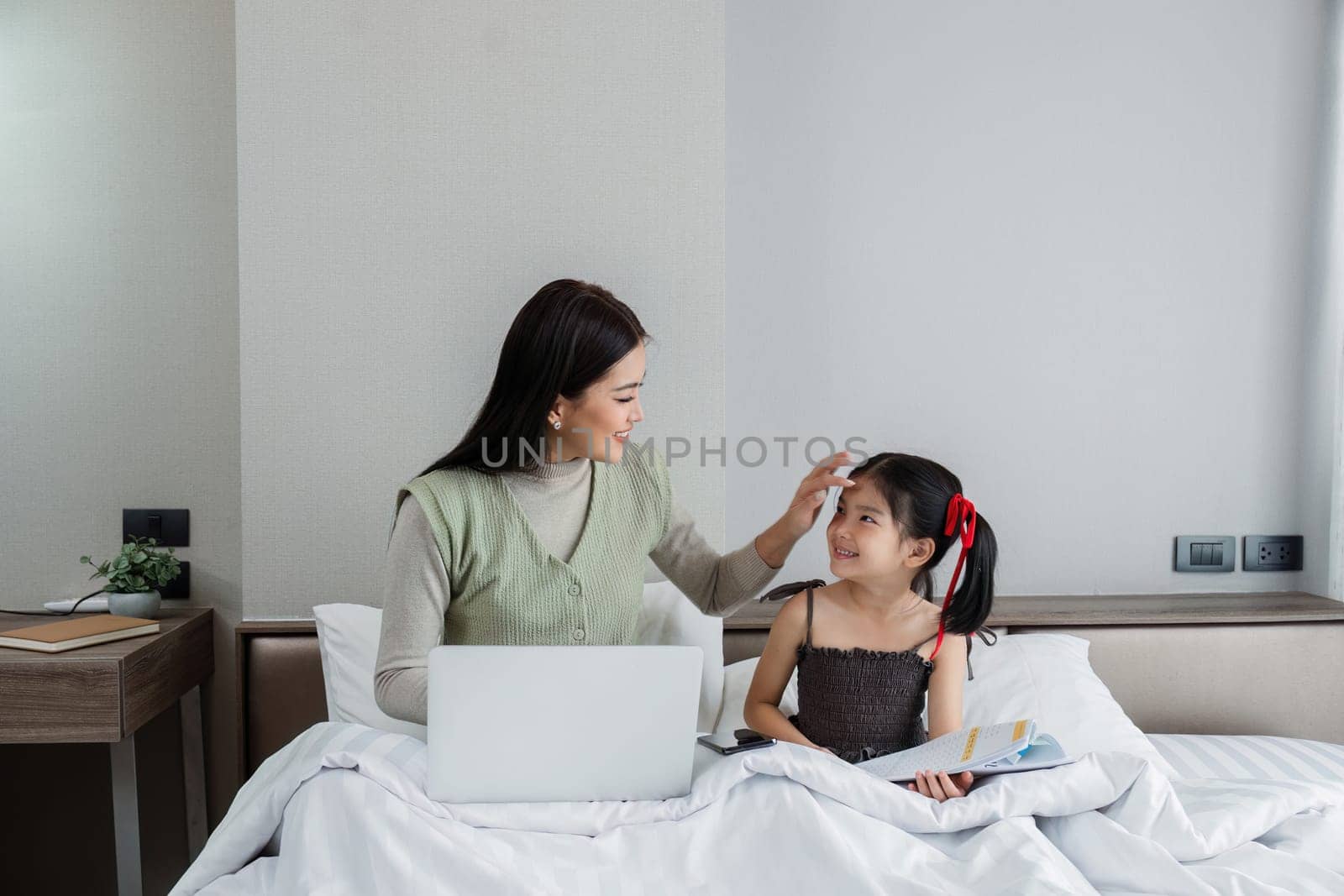 Work from home, freelance and lifestyle concept. Portrait of creative asian female sitting on bed with laptop and her take care of her kid while working.