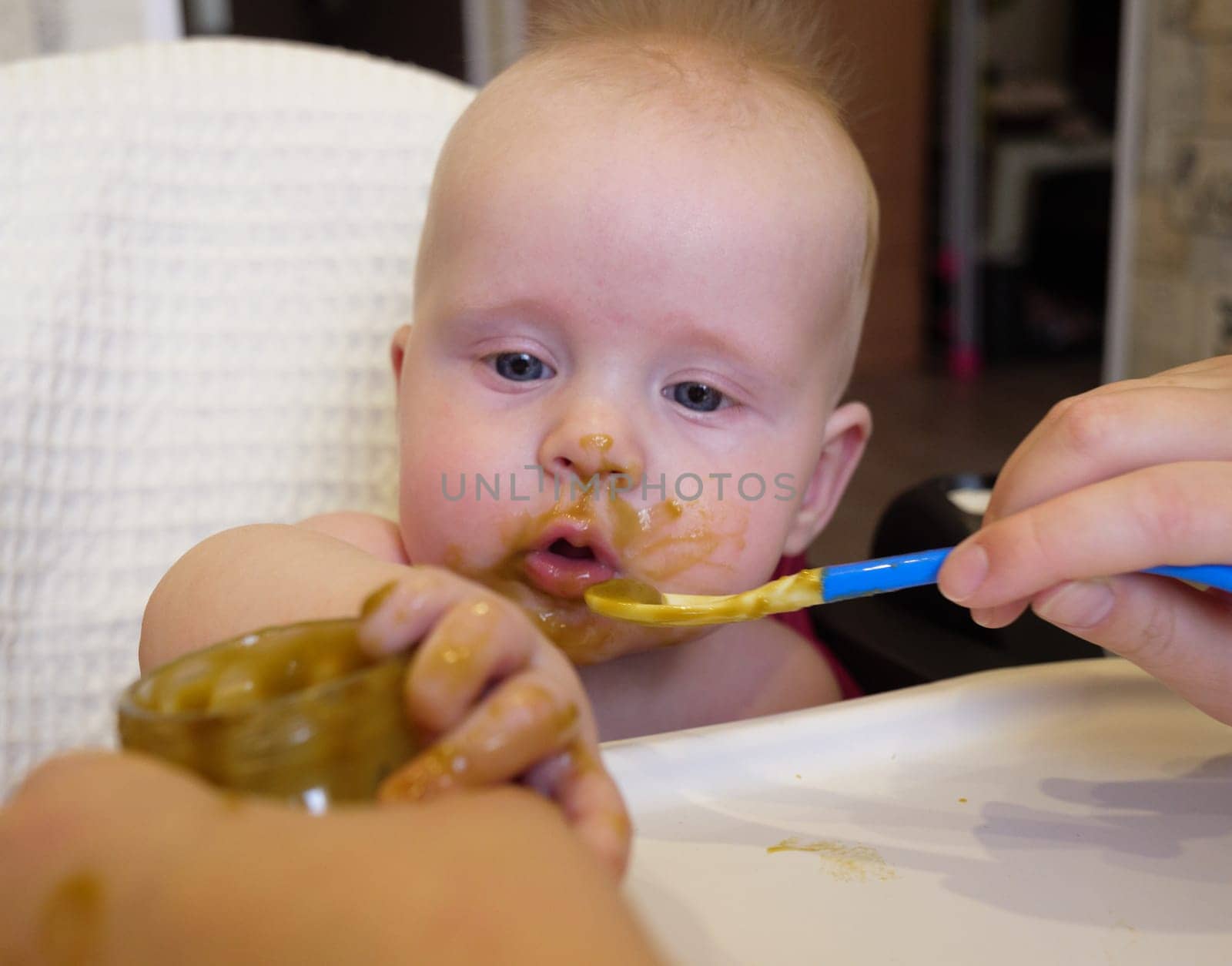 Mom feeding little boy with broccoli puree. Child at the age of six months eats broccoli while sitting on a baby chair.
