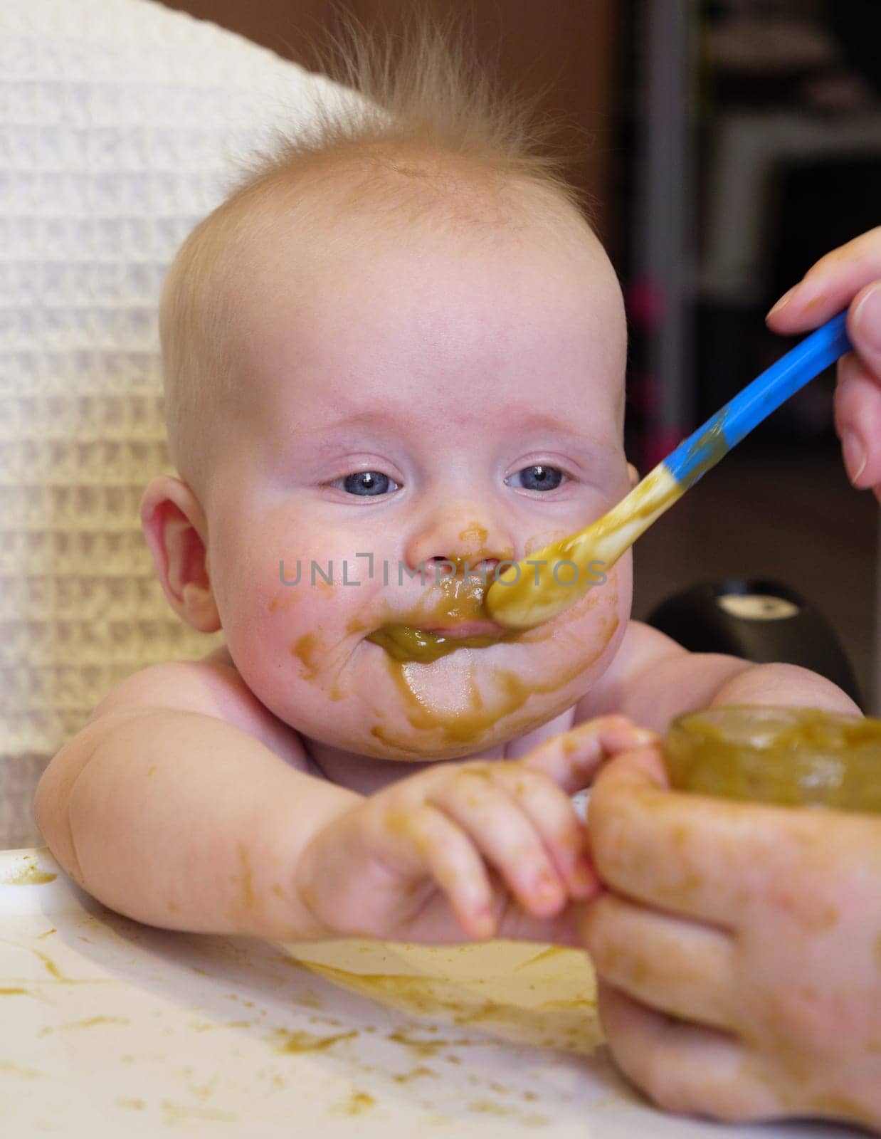 Mom feeding little boy with broccoli puree. Child at the age of six months eats broccoli while sitting on a baby chair.