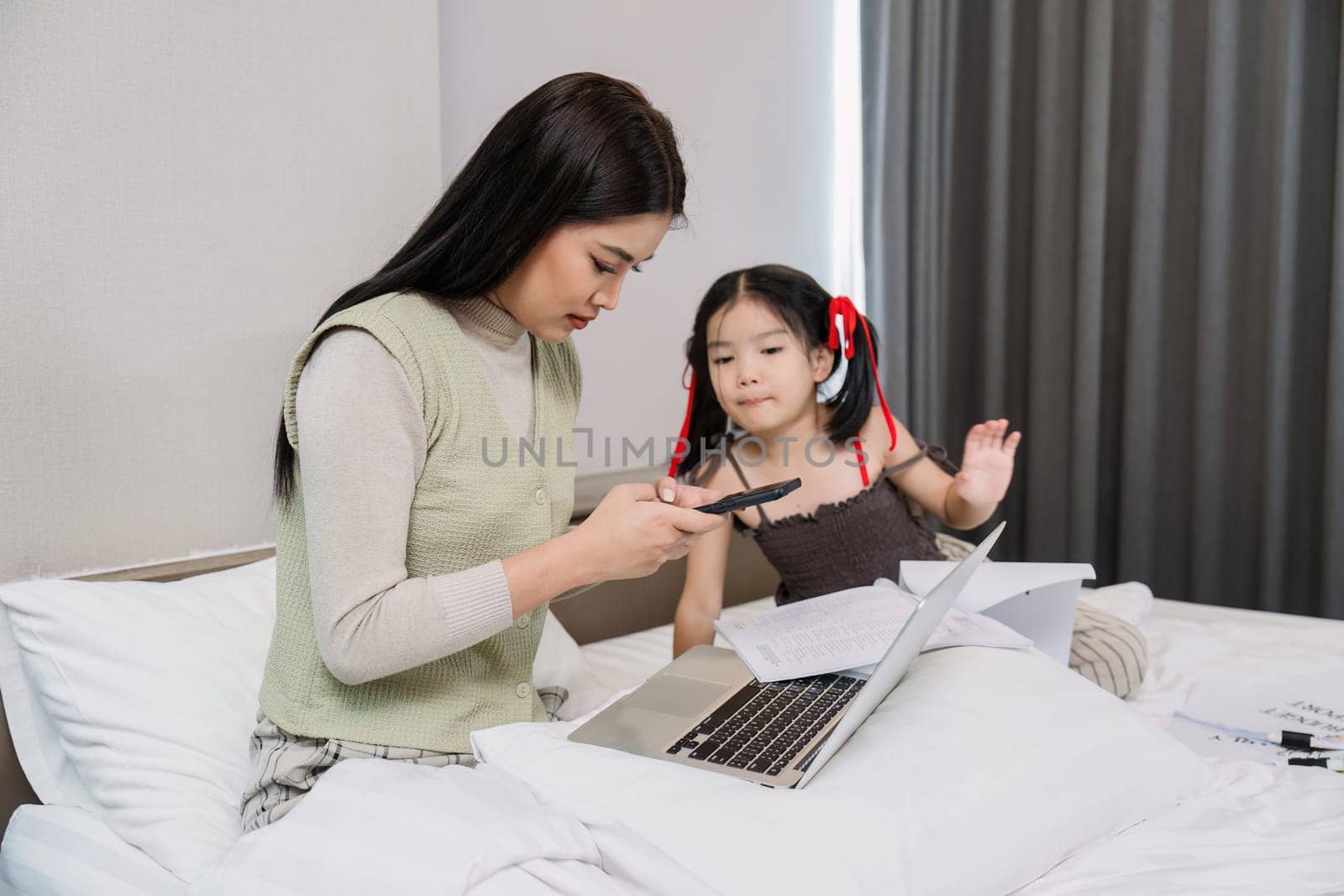 Work from home, freelance and lifestyle concept. Portrait of creative asian female sitting on bed with laptop and her take care of her kid while working.