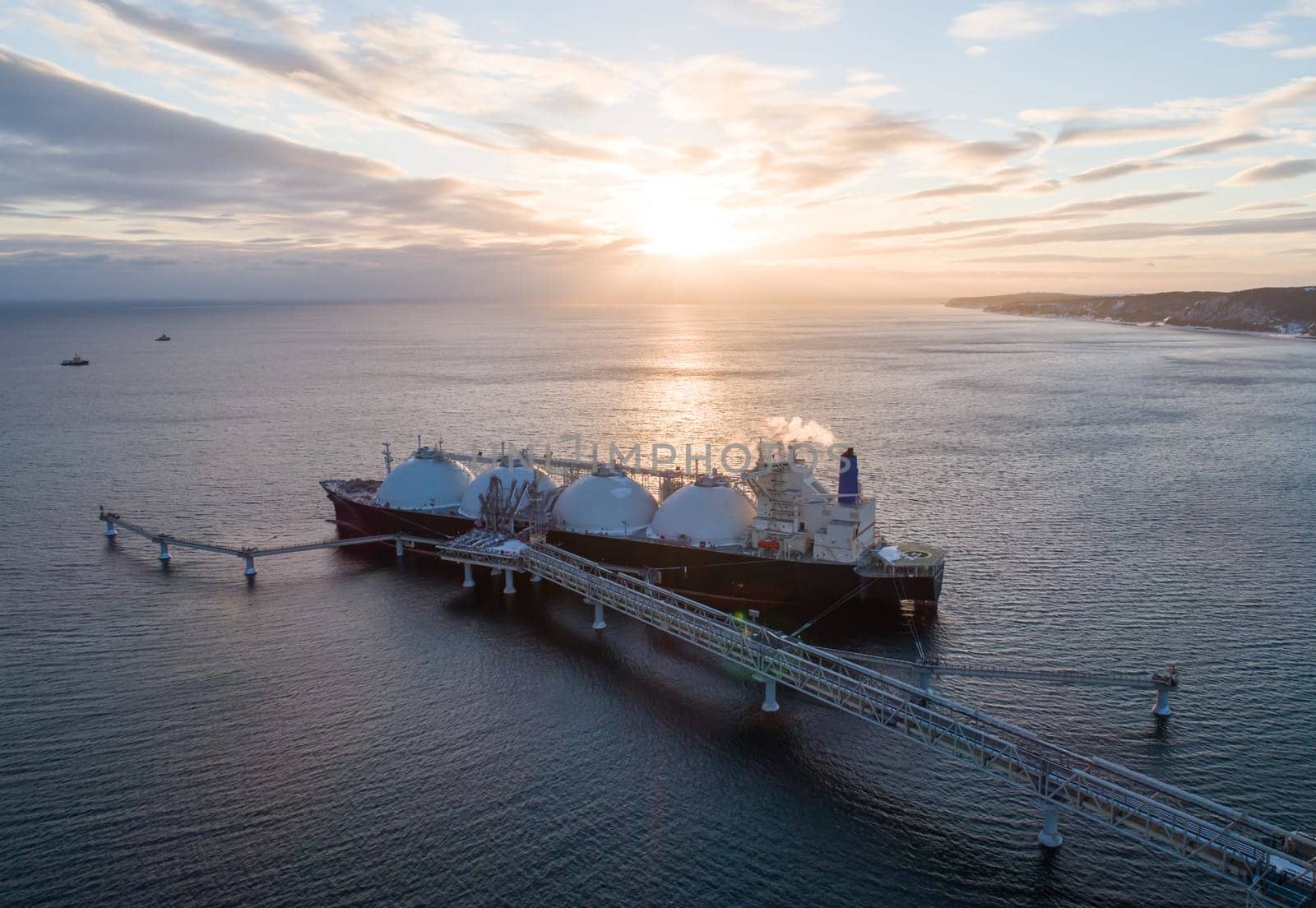 Aerial of Liquified Natural Gas LNG carrier moored to a small gas terminal. Fuel crisis. Sanctions. Wide panoramic shot.