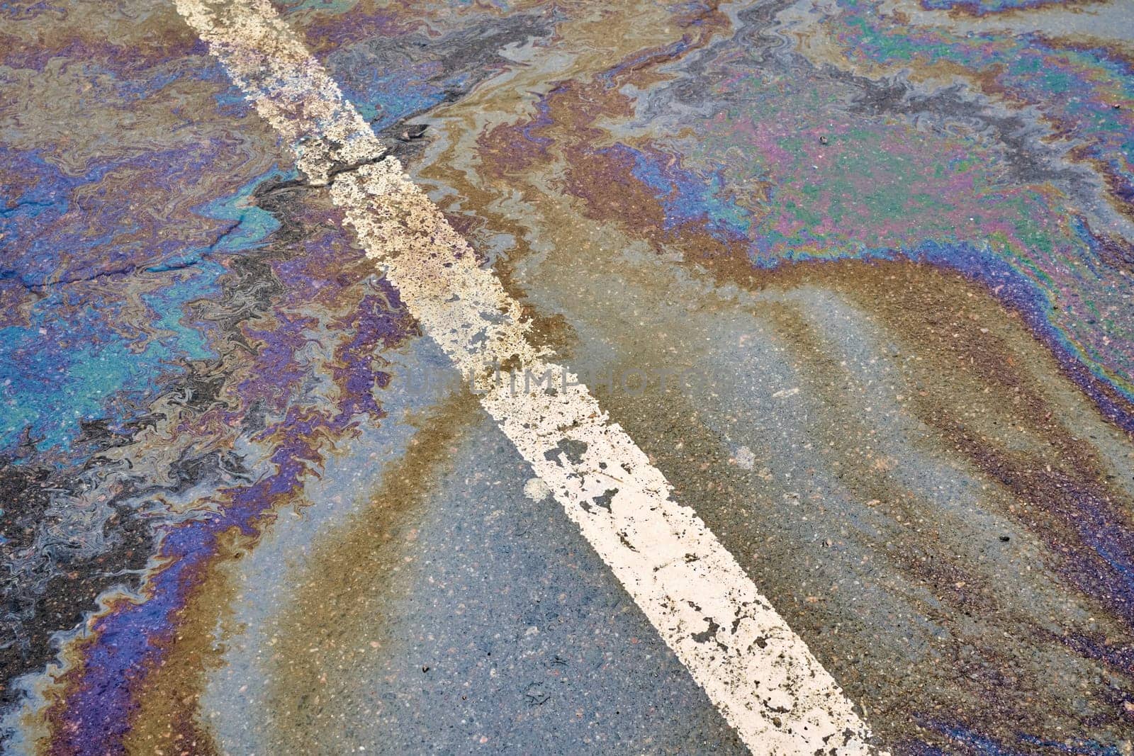 Oil spill on wet asphalt, parking lot with dividing line. Environmental problems of water pollution