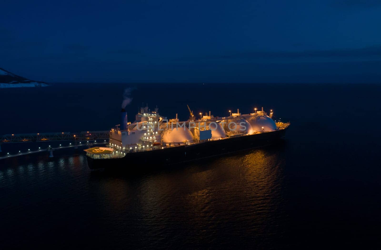 Aerial of Liquified Natural Gas LNG carrier moored to a small gas terminal at dusk. Fuel crisis. Sanctions.