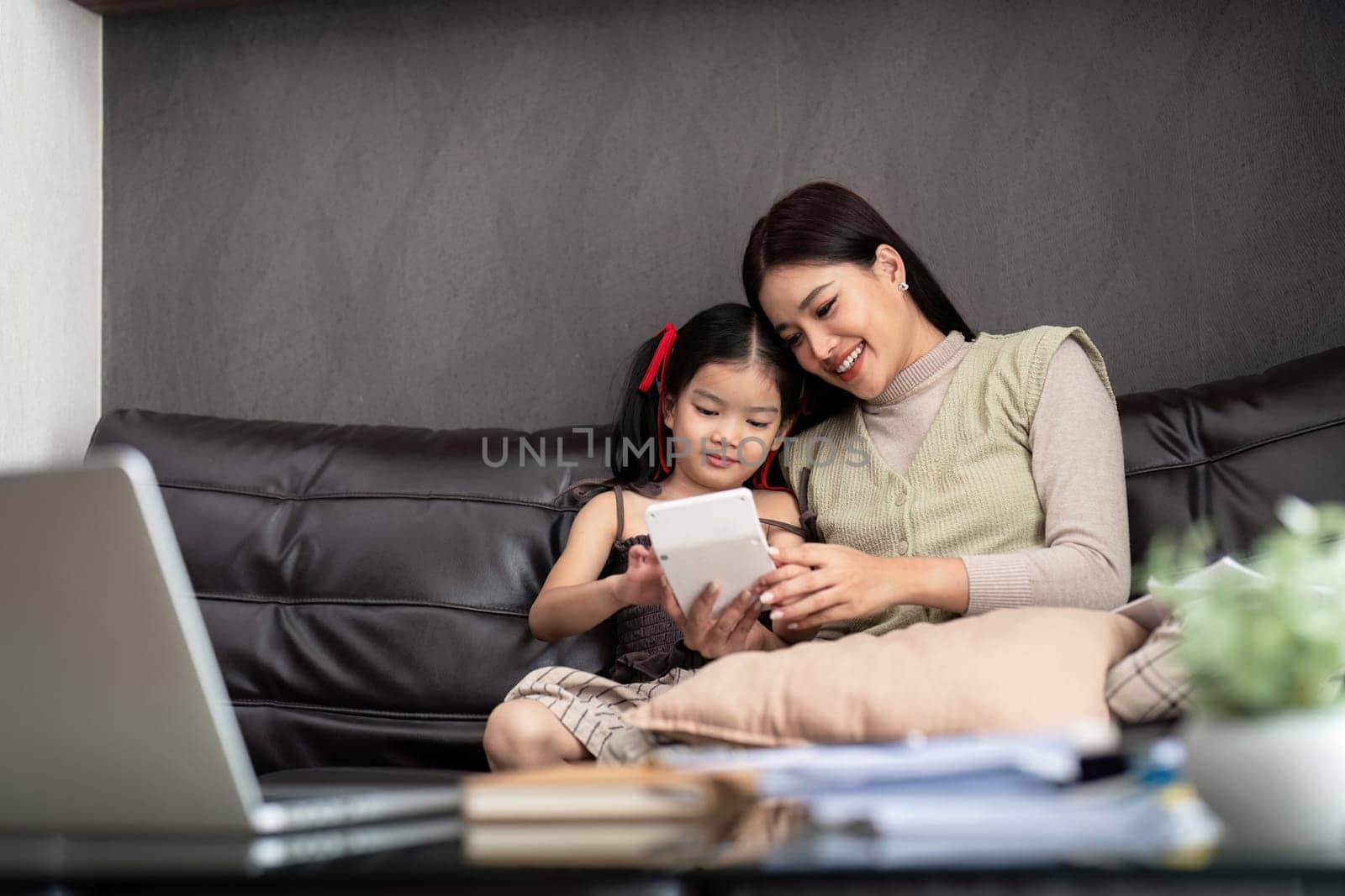 Business woman or mom working with her little daughter at a laptop. Freelance, work from home.