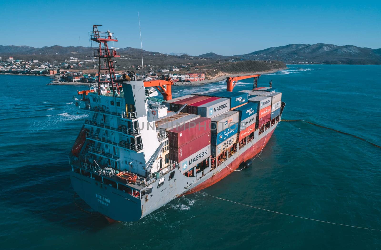 Nakhodka, Russia - November 13, 2021: Aerial view of a RISE SHINE container cargo ship stands aground after a storm with floating boom around the ship to prevent the spread of petroleum. by Busker