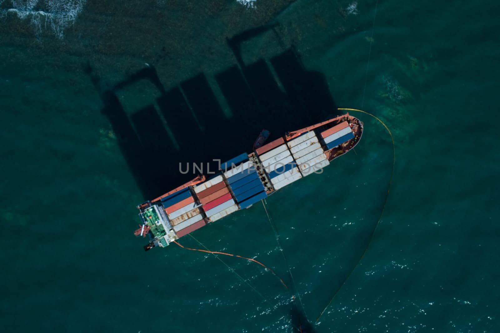 Aerial top down view of a container cargo ship stands aground after a storm with floating boom around the ship to prevent the spread of petroleum..