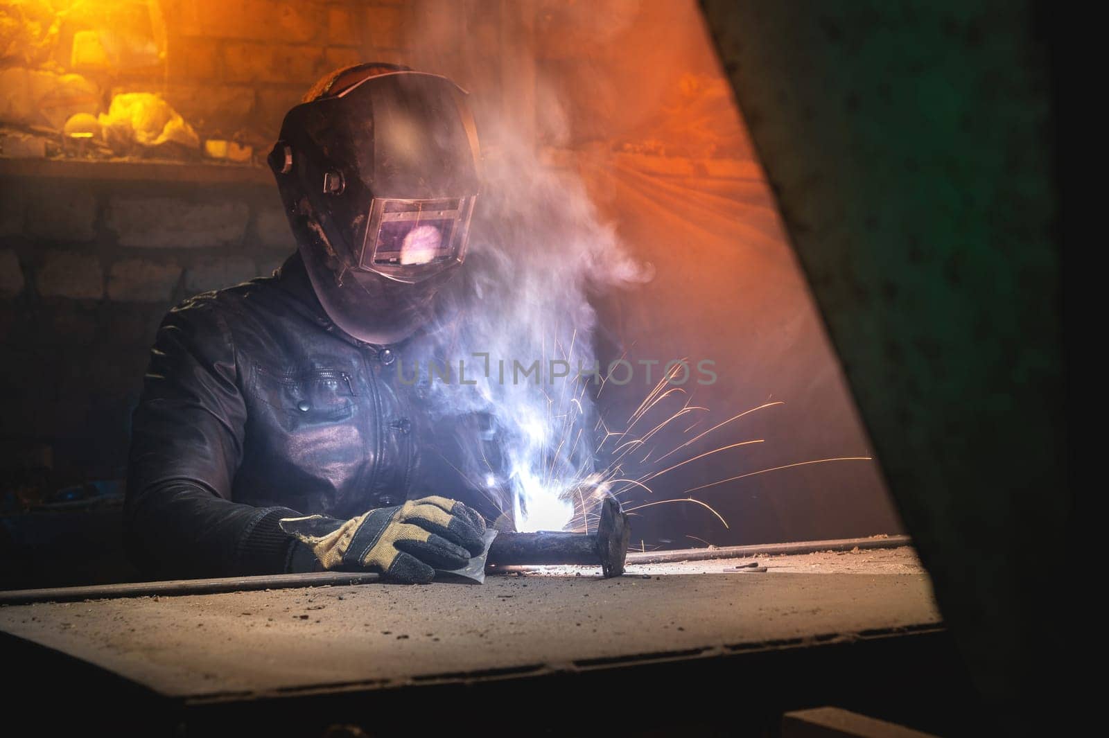 A welder wearing a mask and eye protection welds a part on a pipe. Close-up of an old trowel and individual work.