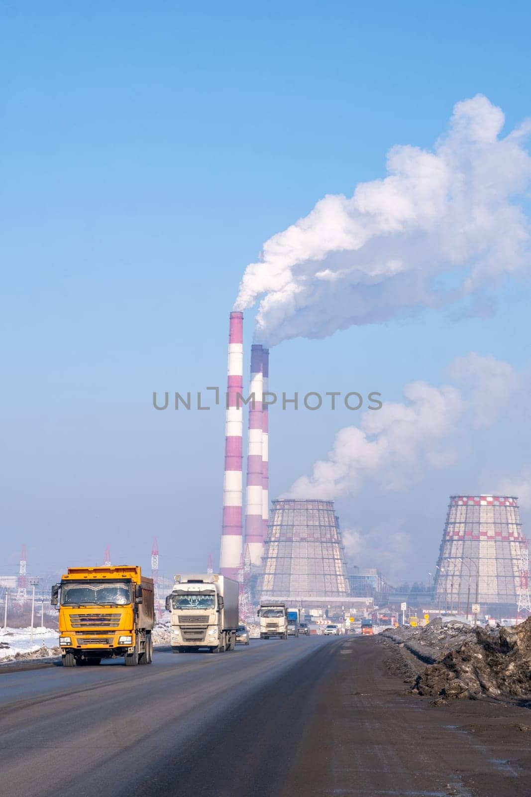 Row of trucks passing factory with smokestacks, clouds of pollution fill the sky by AnatoliiFoto