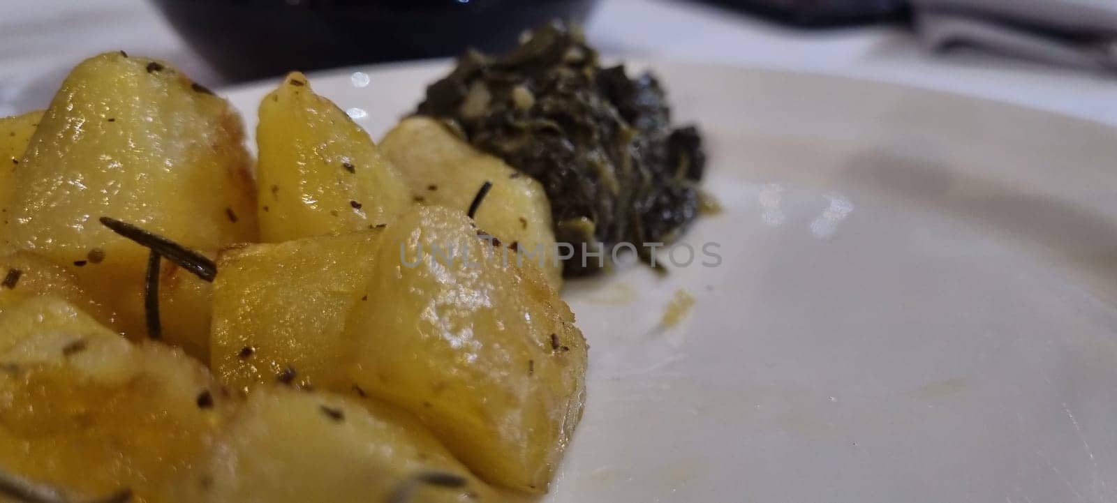 Close-up of herbed roasted potatoes and cooked spinach served on a white plate
