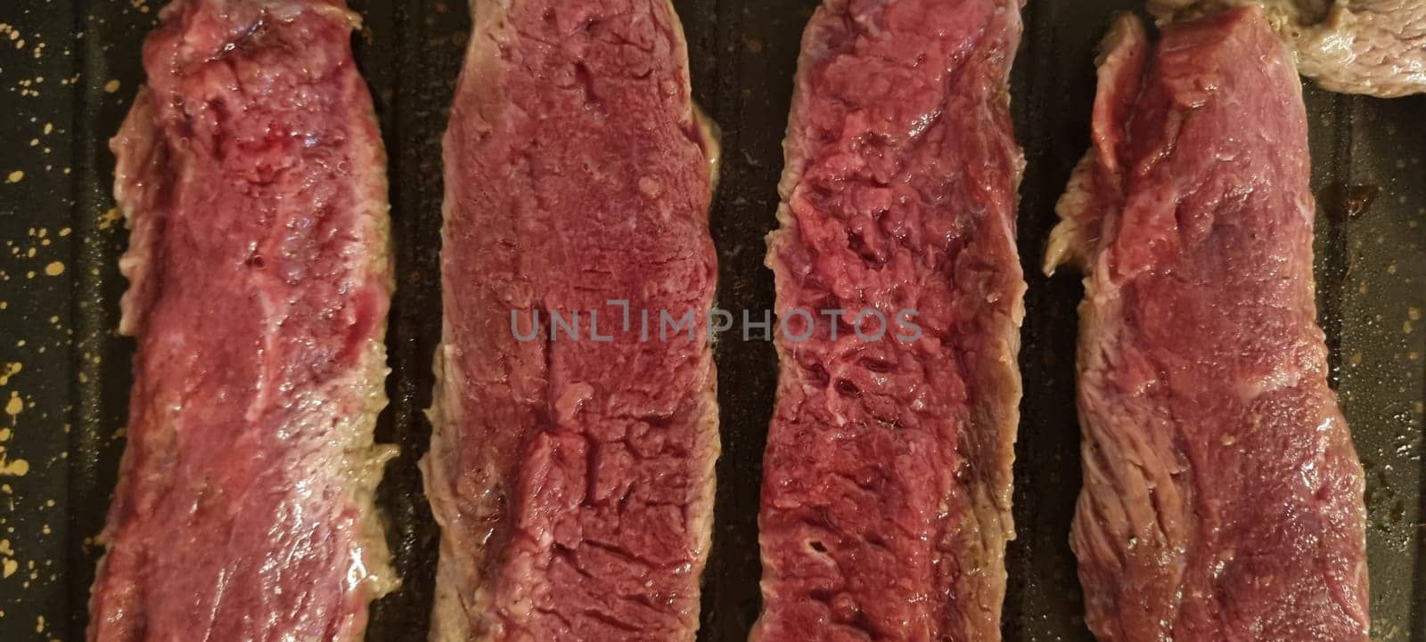 Close-up of raw steak strips seasoned and ready to cook on a dark grill pan