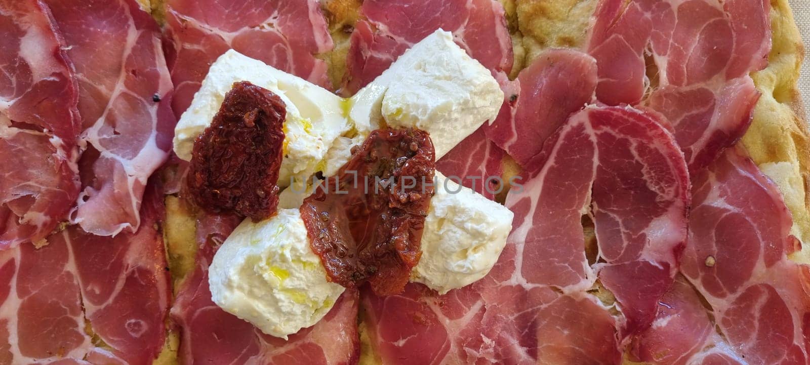 Close-up view of an italian pizza topped with cured ham, fresh mozzarella, and sun-dried tomatoes