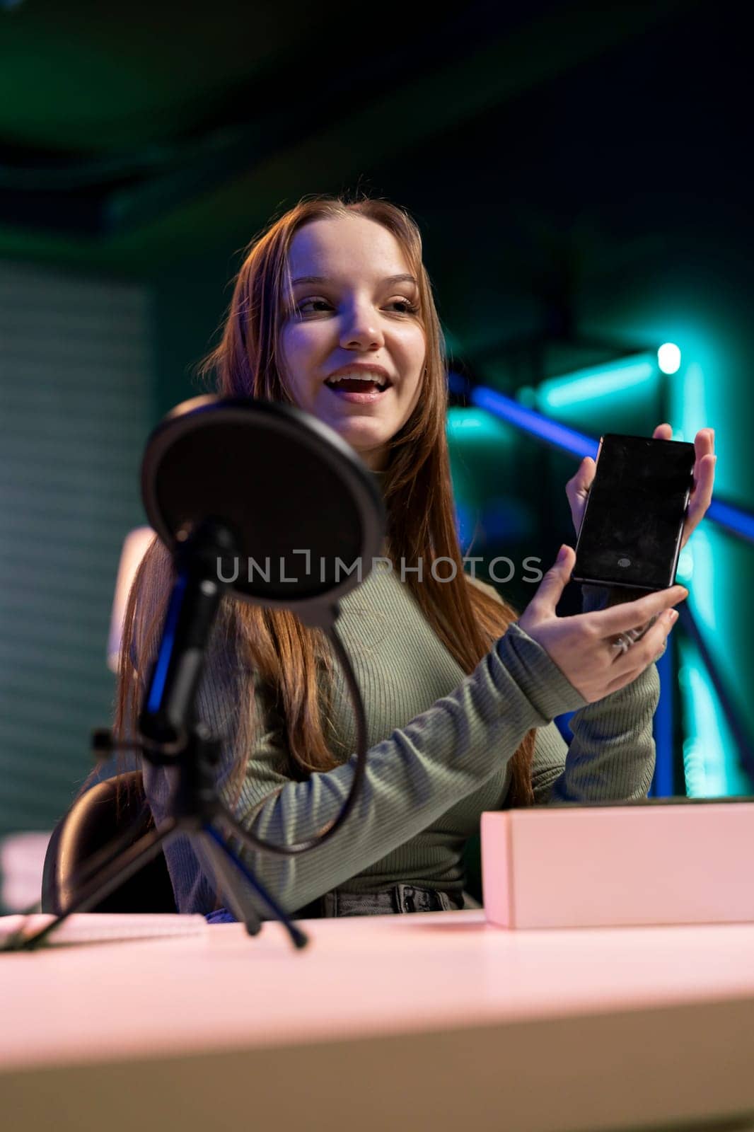 Teenager content creator filming technology review of newly released smartphone, unpacking it and presenting specifications to audience. Media star showing cellphone to fans from studio