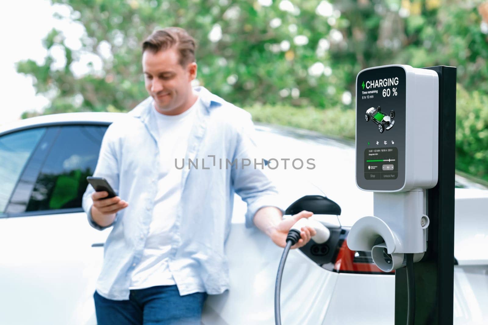 Modern eco man recharge EV car with smartphone. Synchronos by biancoblue