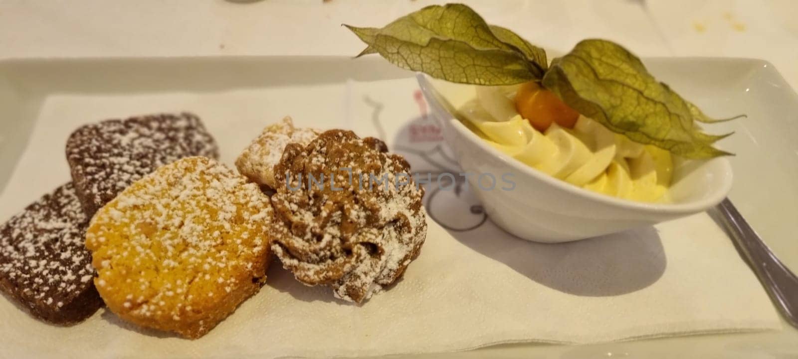 Delicious selection of mini pastries dusted with sugar, served with fresh whipped cream on a white plate